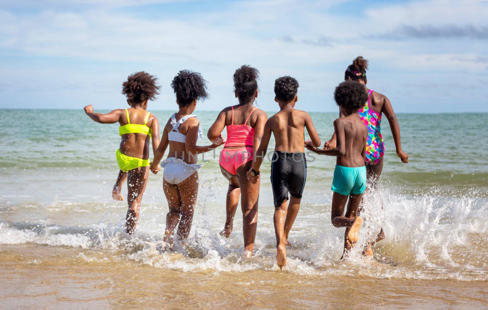 Kids playing running on sand at the beach, A group of children holding hands in a row on the beach in summer, rear view against sea and blue sky