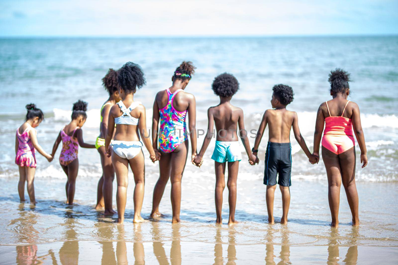 Kids playing running on sand at the beach, A group of children holding hands in a row on the beach in summer, rear view against sea and blue sky