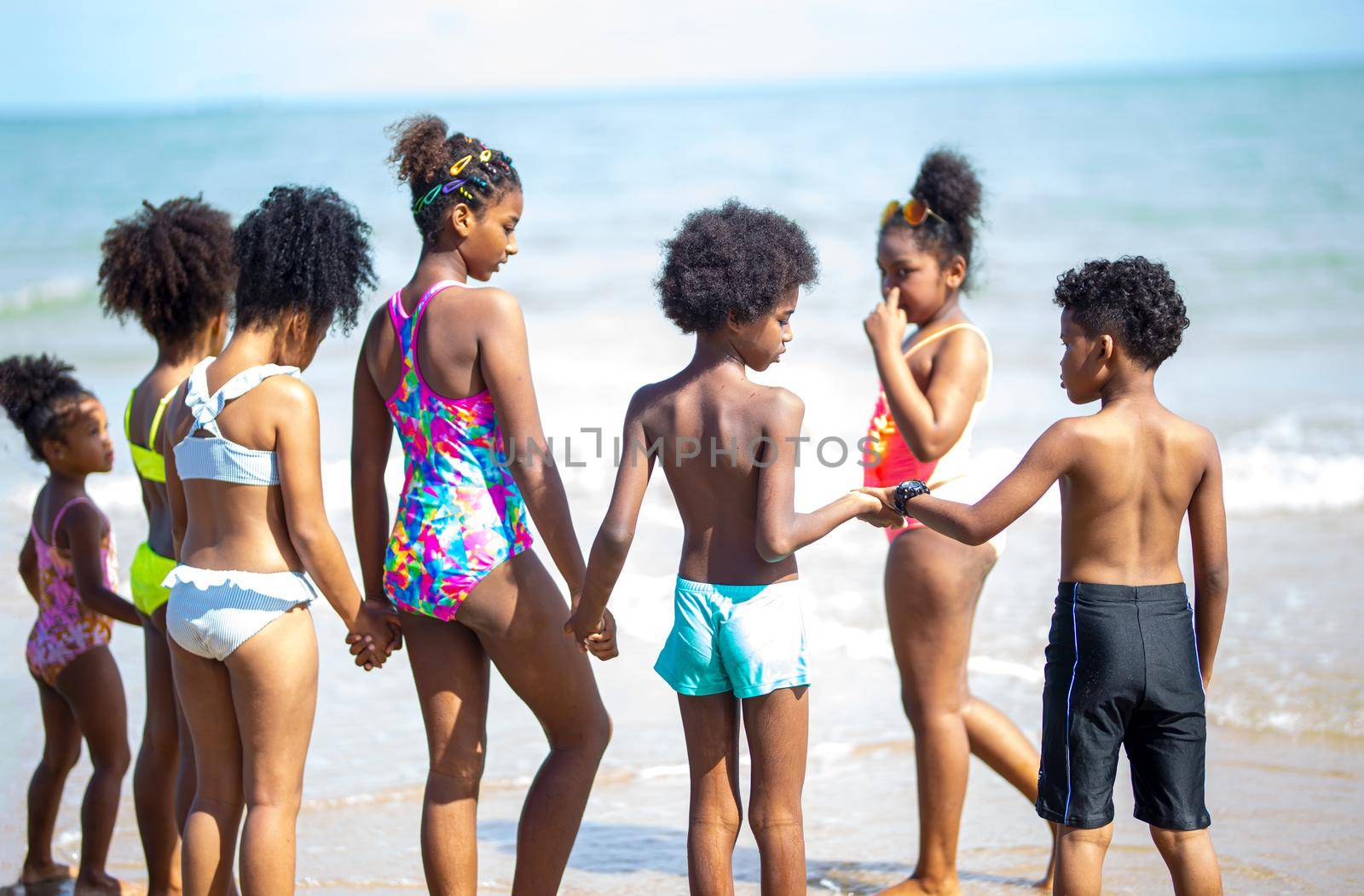 Kids playing running on sand at the beach, A group of children holding hands in a row on the beach in summer, rear view against sea and blue sky