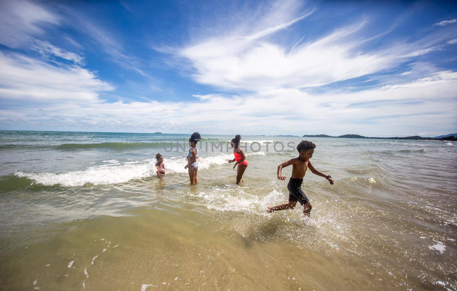 Kids playing running on sand at the beach, A group of children holding hands in a row on the beach in summer, rear view against sea and blue sky