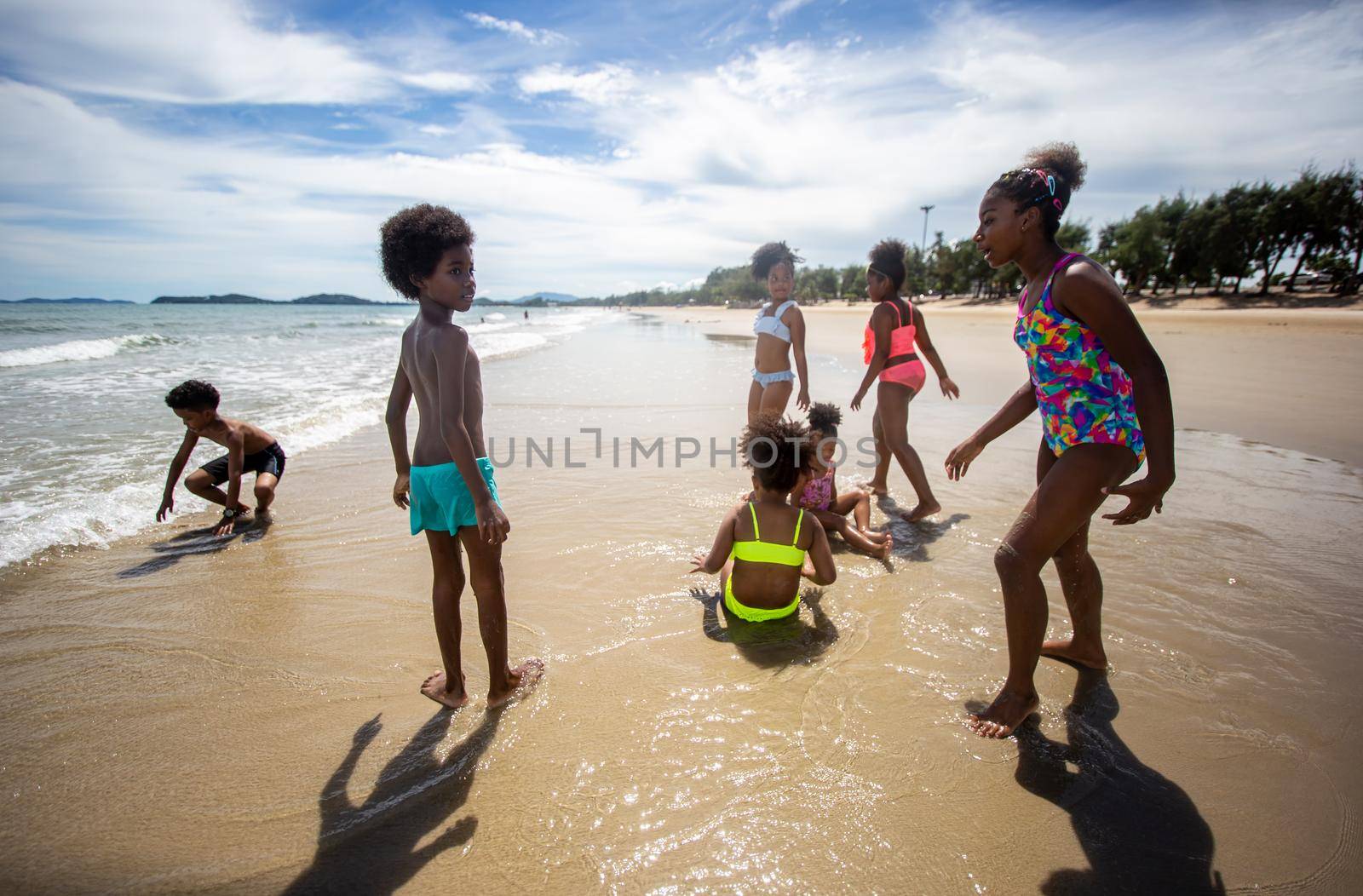Kids playing running on sand at the beach, A group of children holding hands in a row on the beach in summer, rear view against sea and blue sky