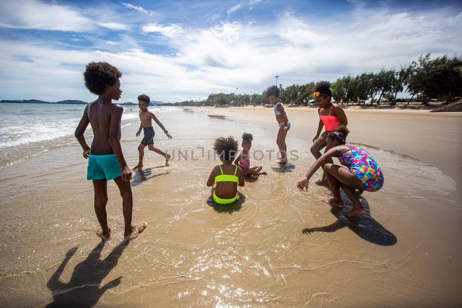 Kids playing running on sand at the beach, A group of children holding hands in a row on the beach in summer, rear view against sea and blue sky