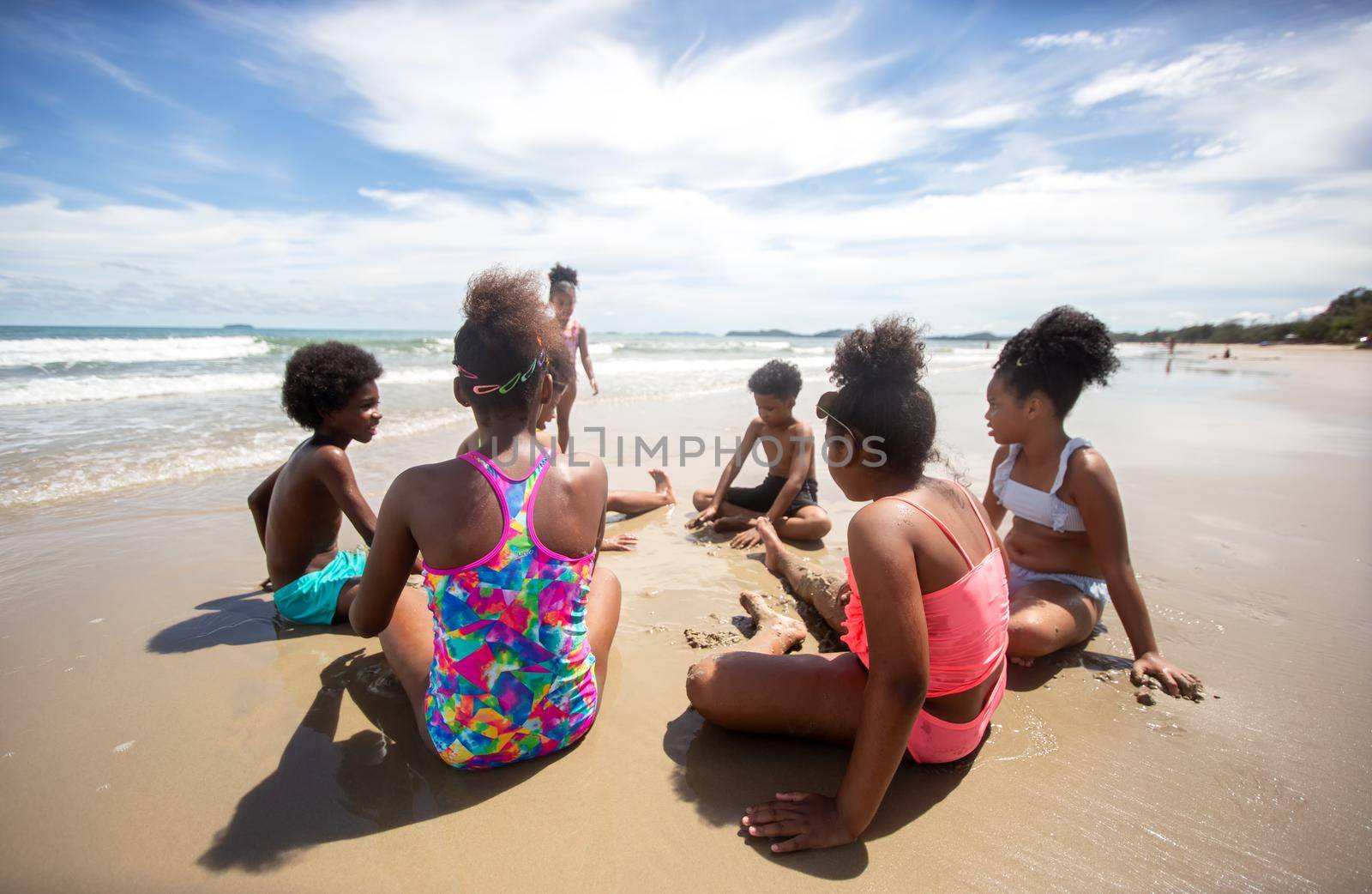 Kids playing running on sand at the beach, A group of children holding hands in a row on the beach in summer, rear view against sea and blue sky