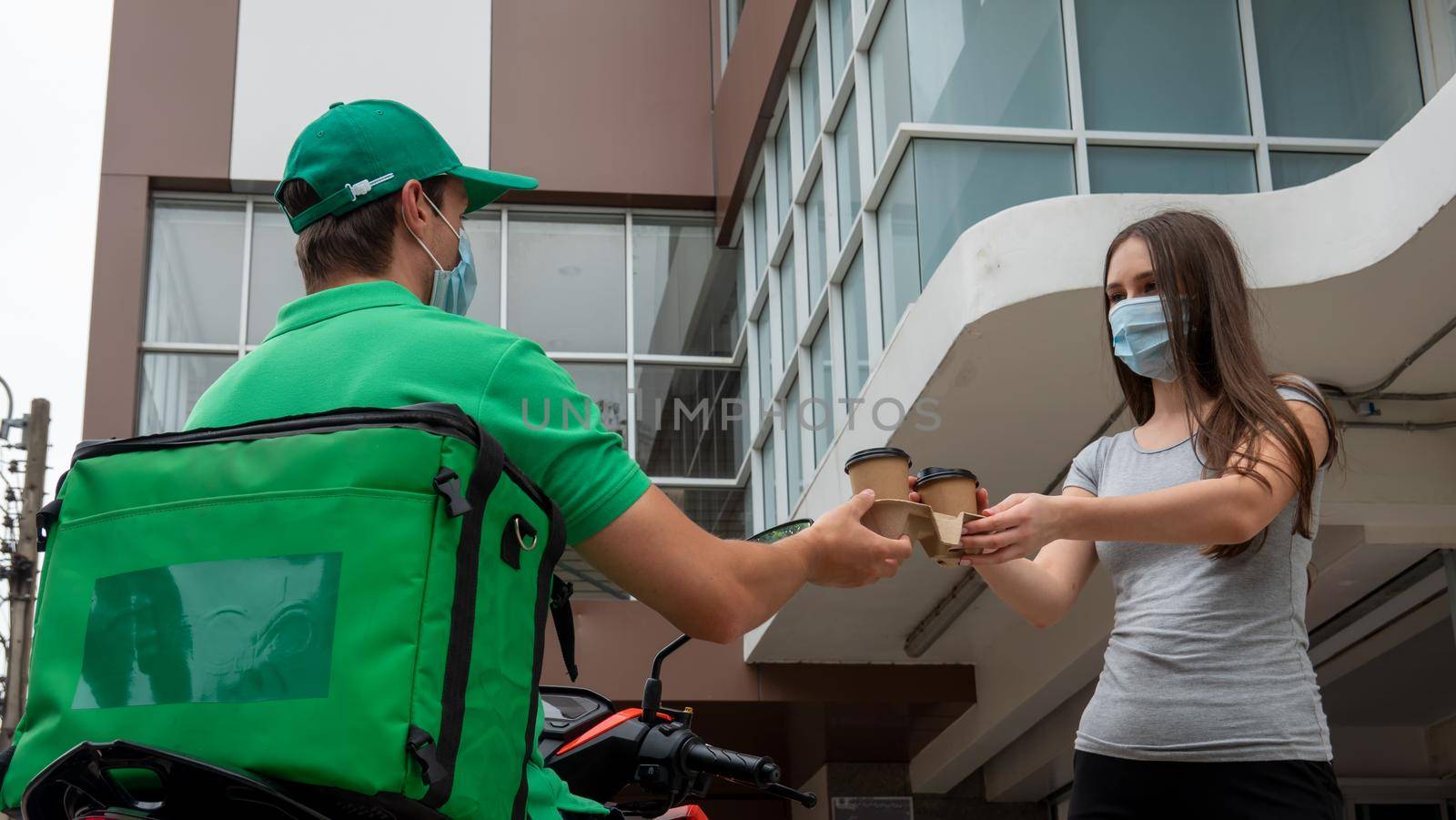 Young man delivering food to customer at doorway, Paper pocket and food containers in hands of a smiling deliveryman outdoors. Quality service of a restaurant.