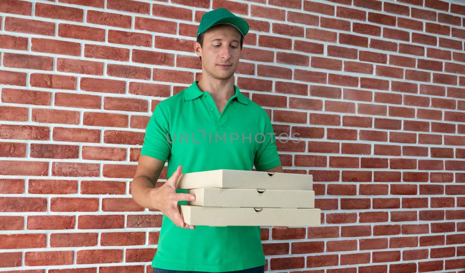 Young man delivering food to customer at doorway, Paper pocket and food containers in hands of a smiling deliveryman outdoors. Quality service of a restaurant.