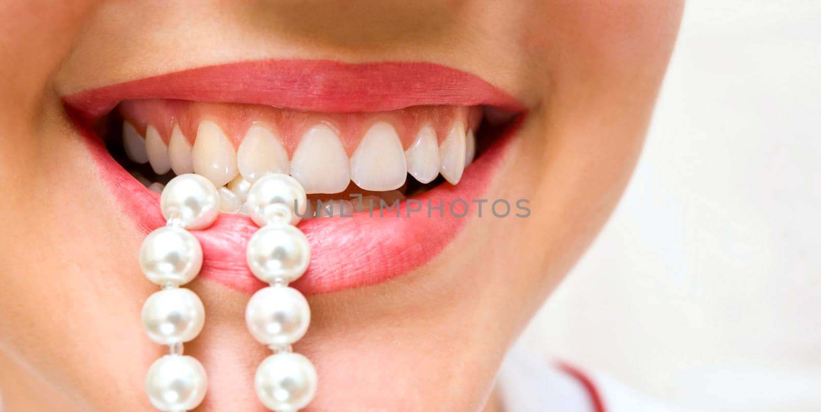 a woman smiles showing white teeth, holding a pearly necklace in to the mouth