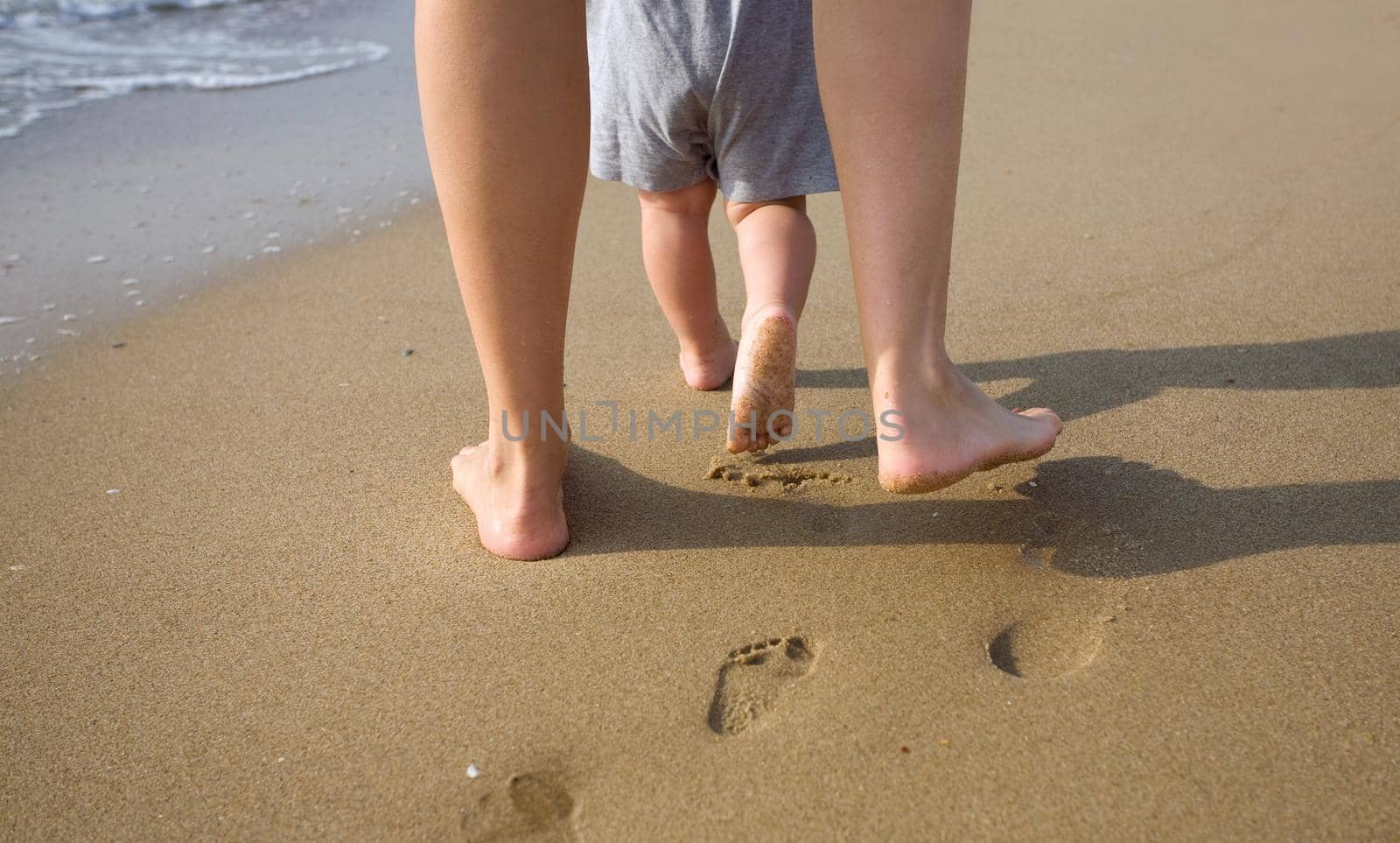 Mother and child walking on a sandy beach by kornienko