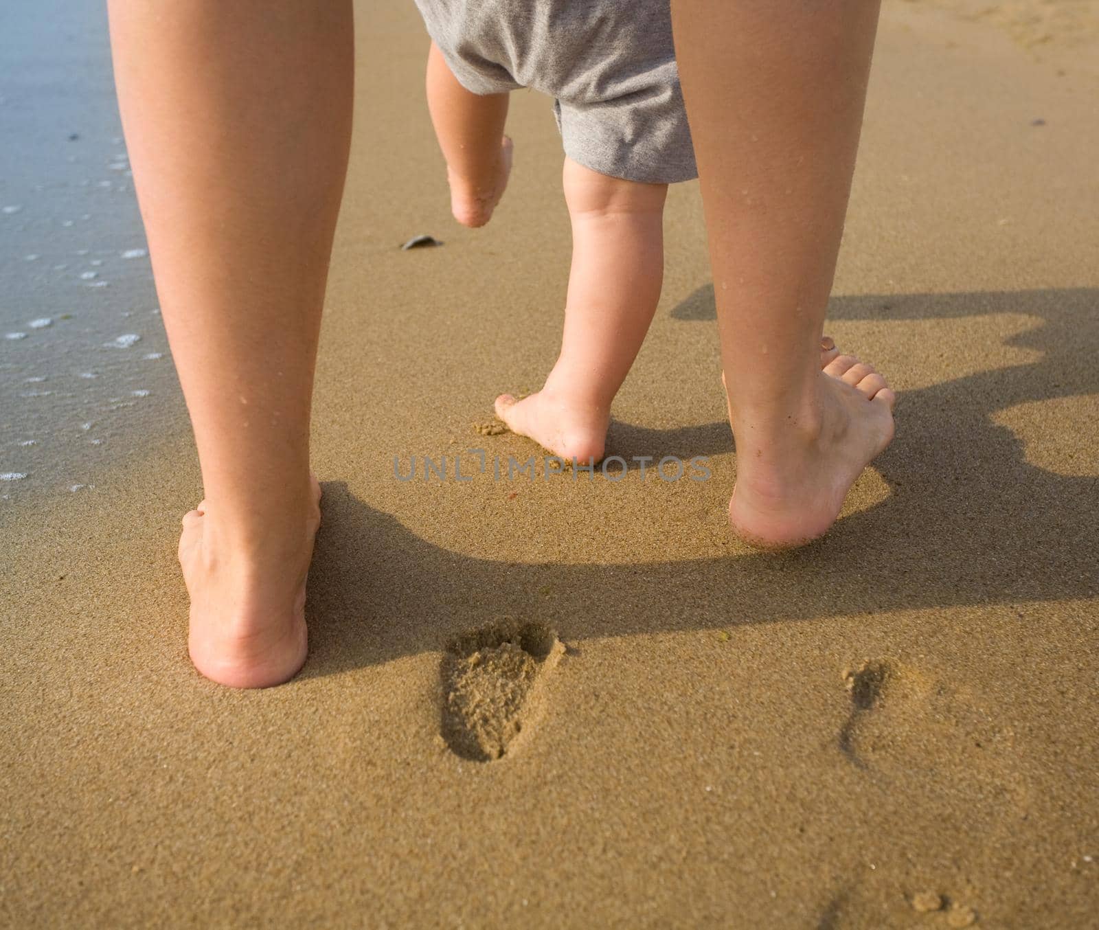 mom helps to make the child's first steps on the beach