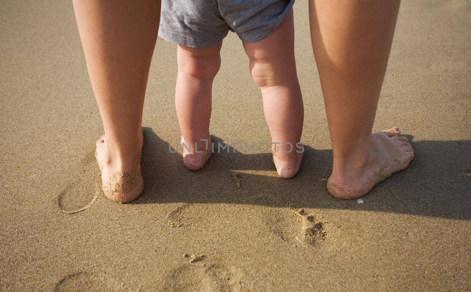 Mother and child walking on a sandy beach by kornienko