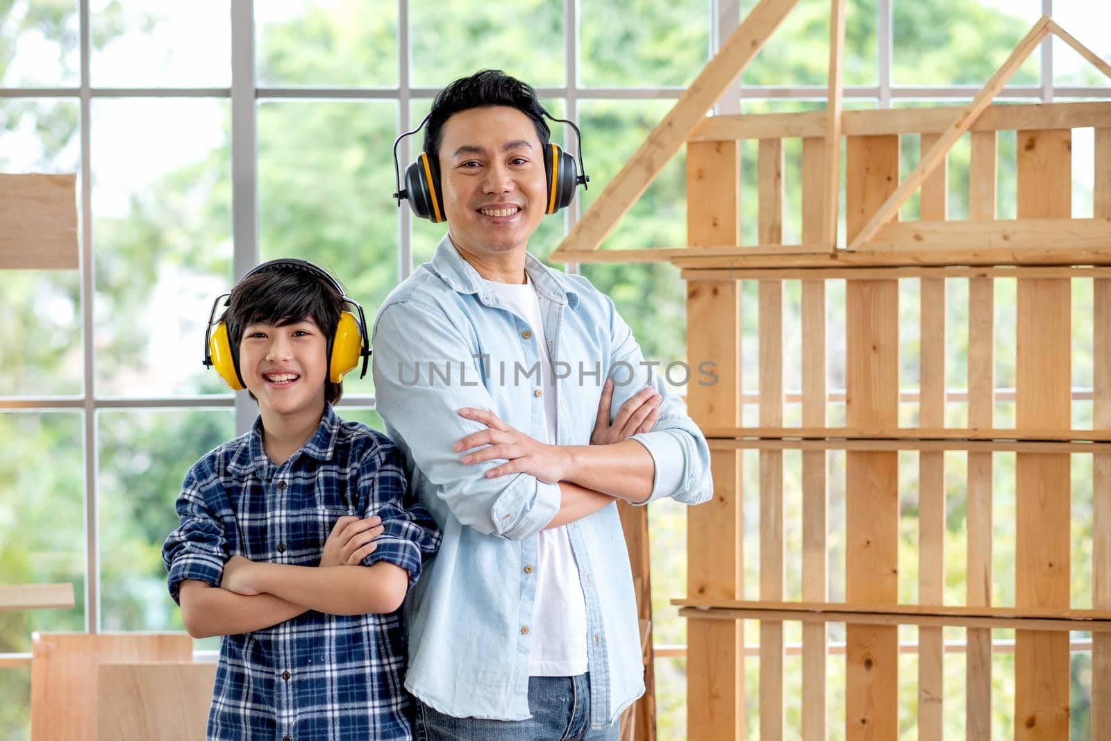 Portrait of Asian father and boy with mechanic headphone stand in front of woodwork and look at camera.