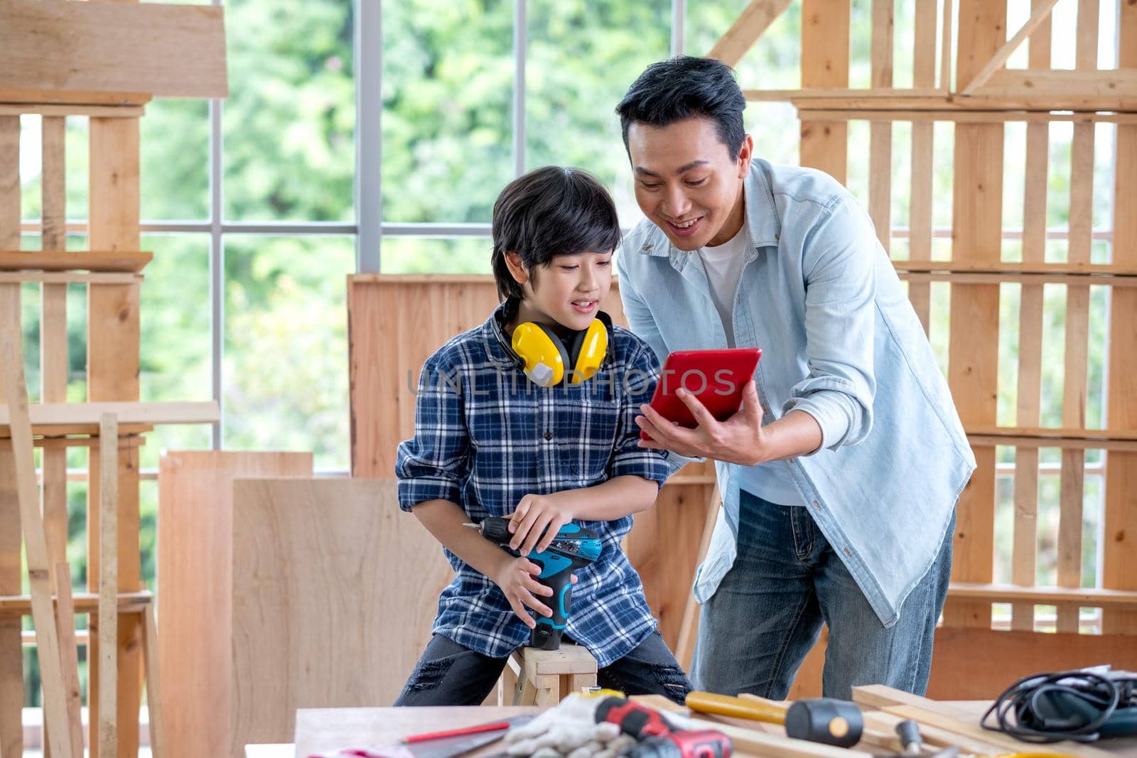 Asian man hold and show tablet to boy and they look happy during carpentering work in their house.