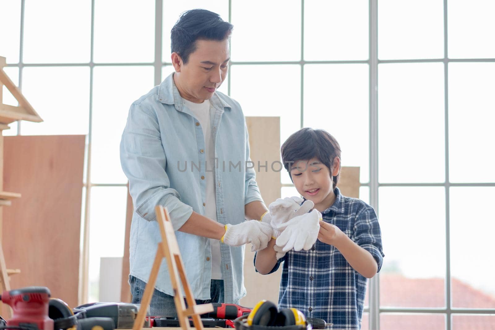 Asian father help his son to wear gloves before work with woodwork in their house. Concept of good relationship with hobby or activities in happy family.