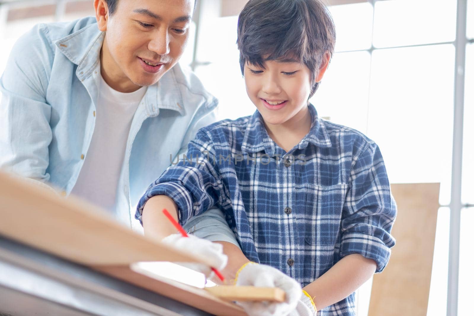 Asian father teach his son to measure and mark with pencil on wood for working with woodwork in their house. Concept of good relationship with hobby or activities in happy family.