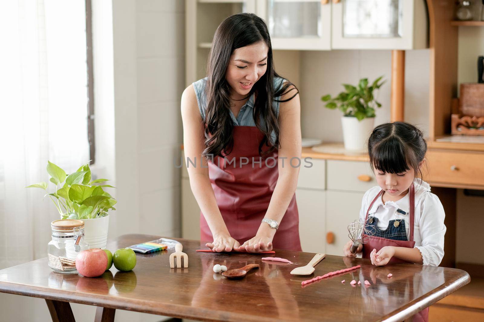 Soft blurred of Asian mother enjoy with play dough together with her daughter in kitchen.