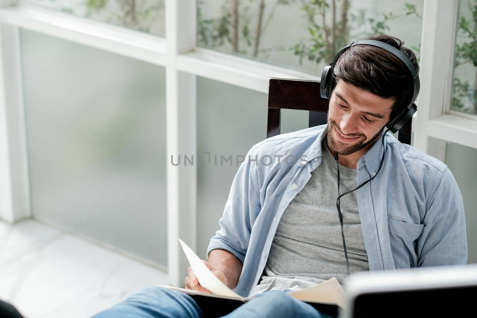 Soft blurred of Caucasian man read book and listen music by headphone with relax and happy expression in room with day light.