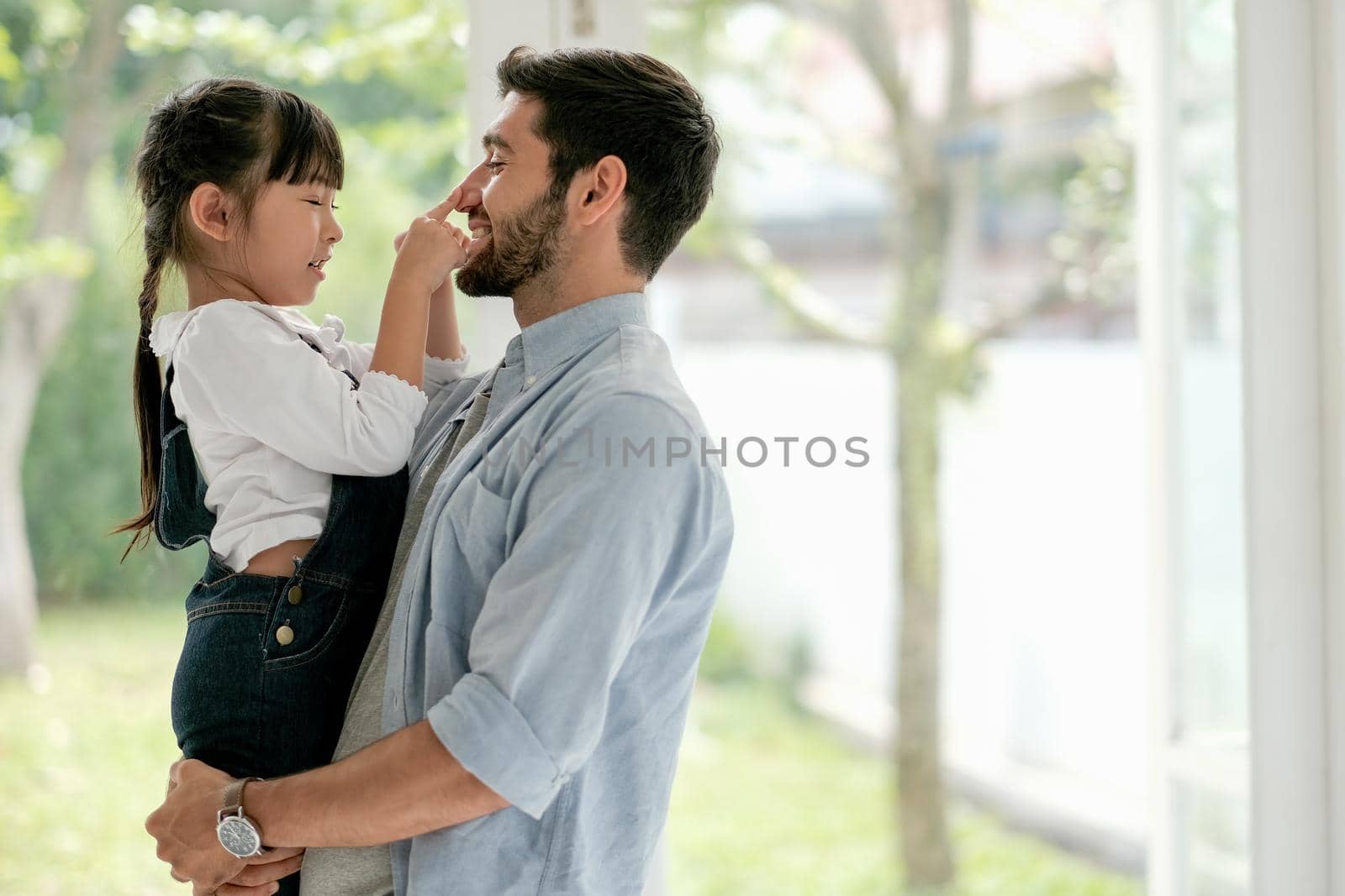 Caucasian man fun to play with his daughter in room with glass windows and they look happy to stay at home during pandemic of Covid-19.