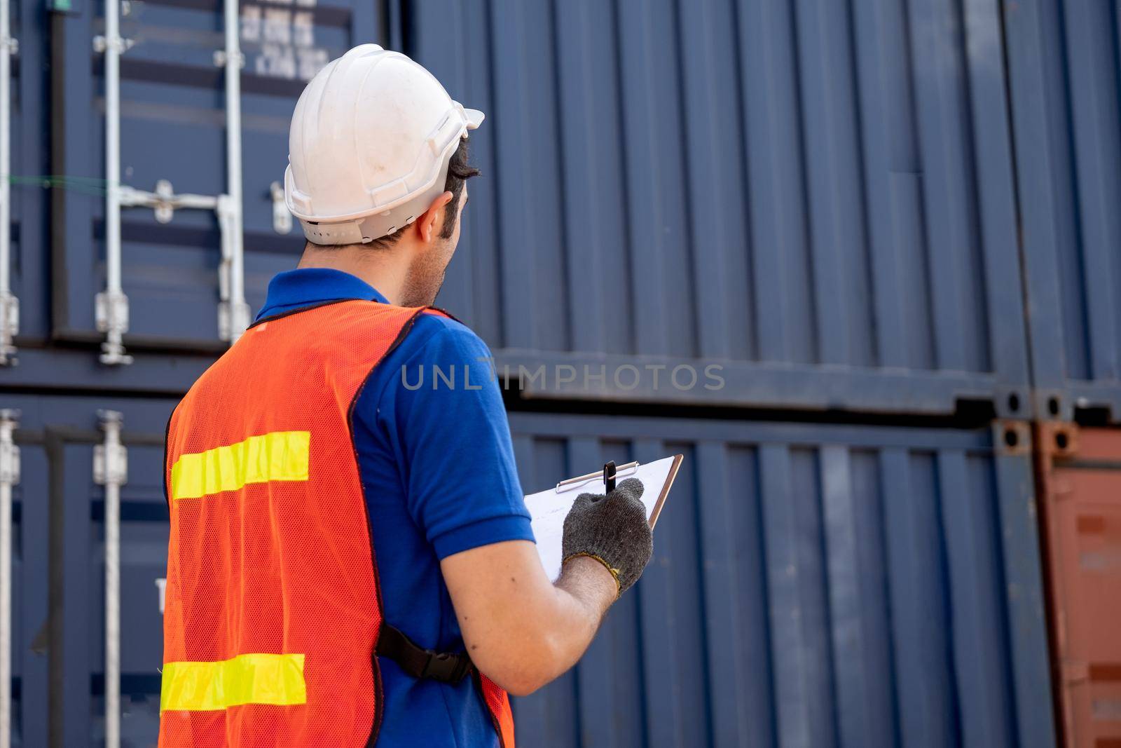 Back of foreman or engineer cargo container worker hold and record data in clipboard and also looking to container tank in workplace area. Industrial data for factory or logistic business concept.