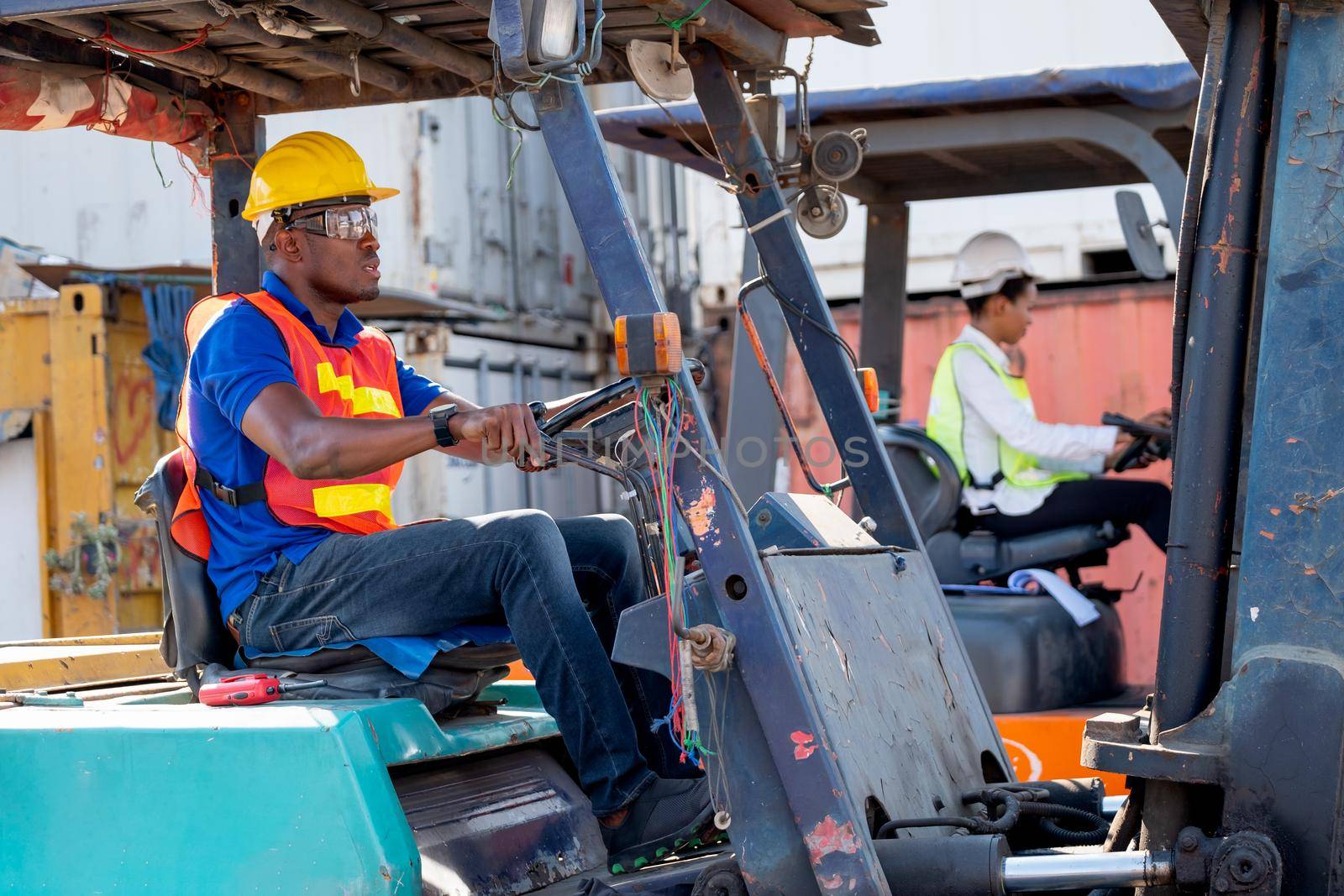 African American foreman or cargo container worker drive cargo car beside of his co-worker woman in workplace area. Industrial support system help employee performance concept.