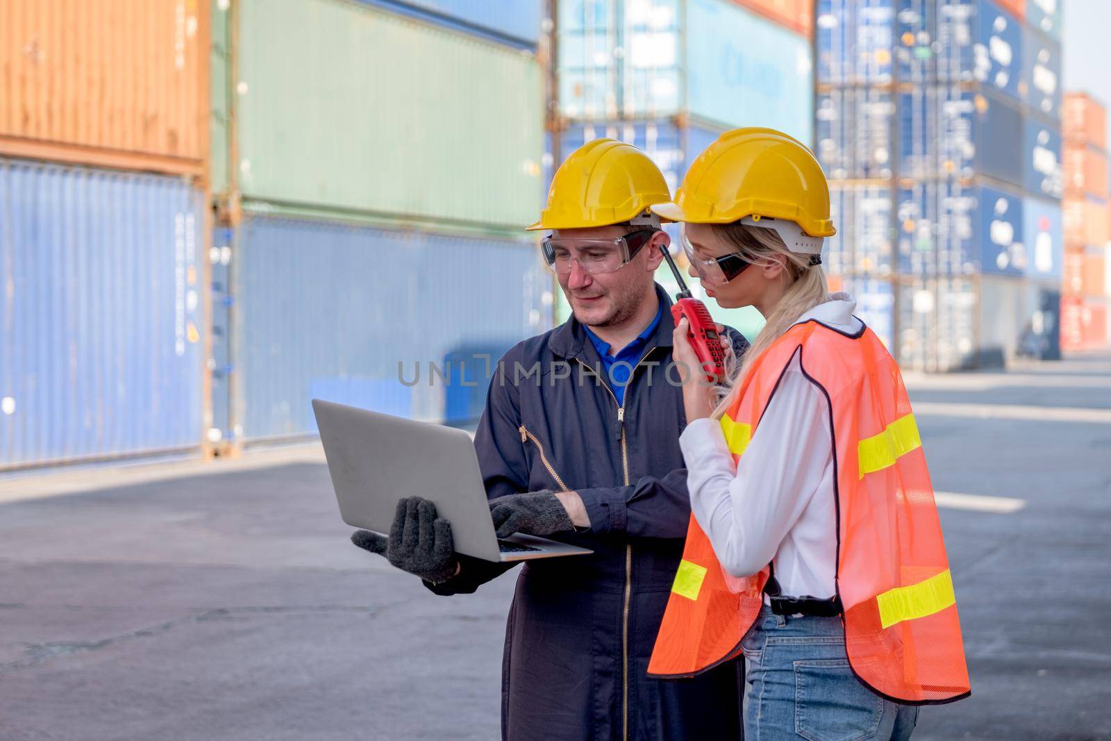 Concept of industrial support work system. Two foreman and cargo container worker discuss together in workplace area with one hold and using laptop and the other hold walkie-talkie to contact team.