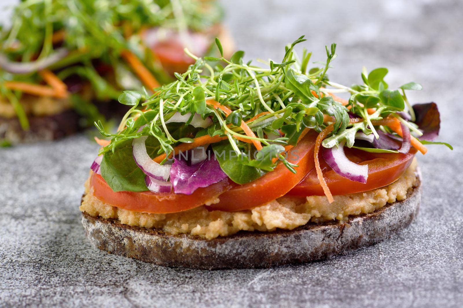 Sandwich toasted rustic bread with chickpea hummus, tomato slices, mix of lettuce and microgreens. Vegetarian breakfast.