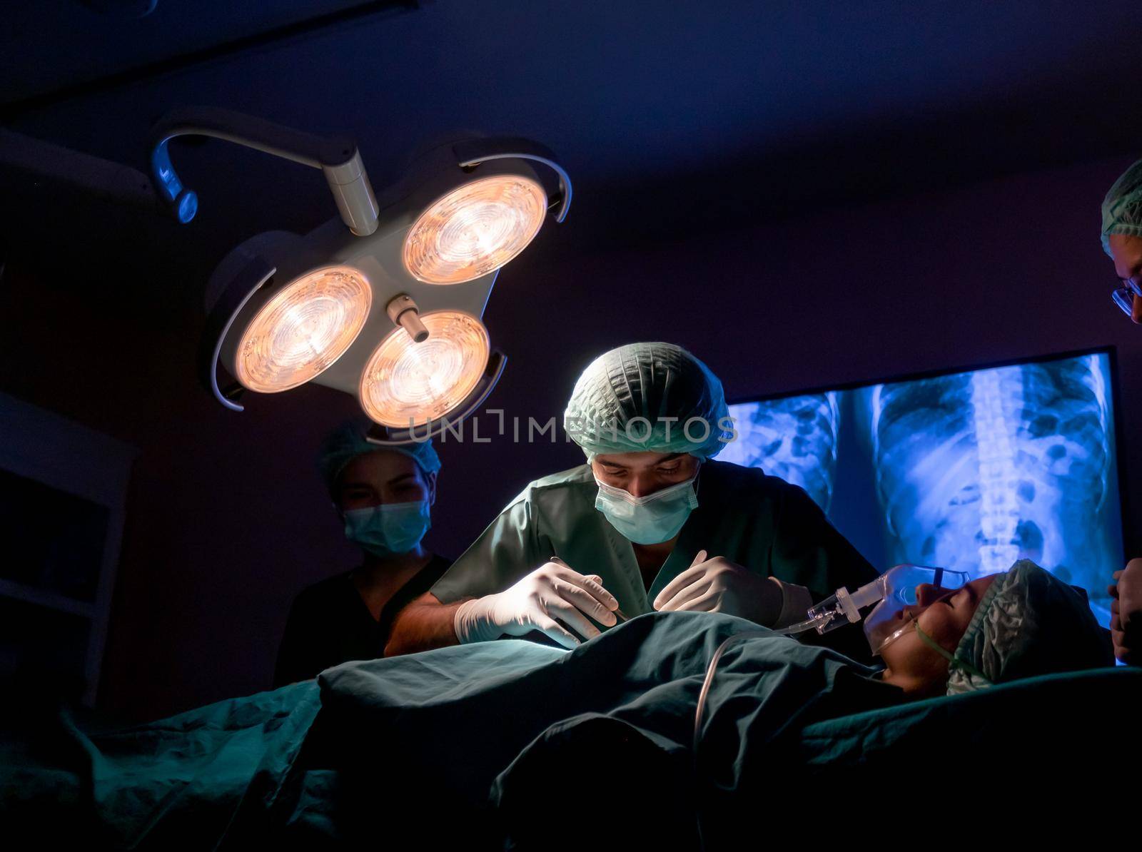 wide shot of operating doctor work on operation of patient with his staff stand to support near him in operating room of clinic or hospital.