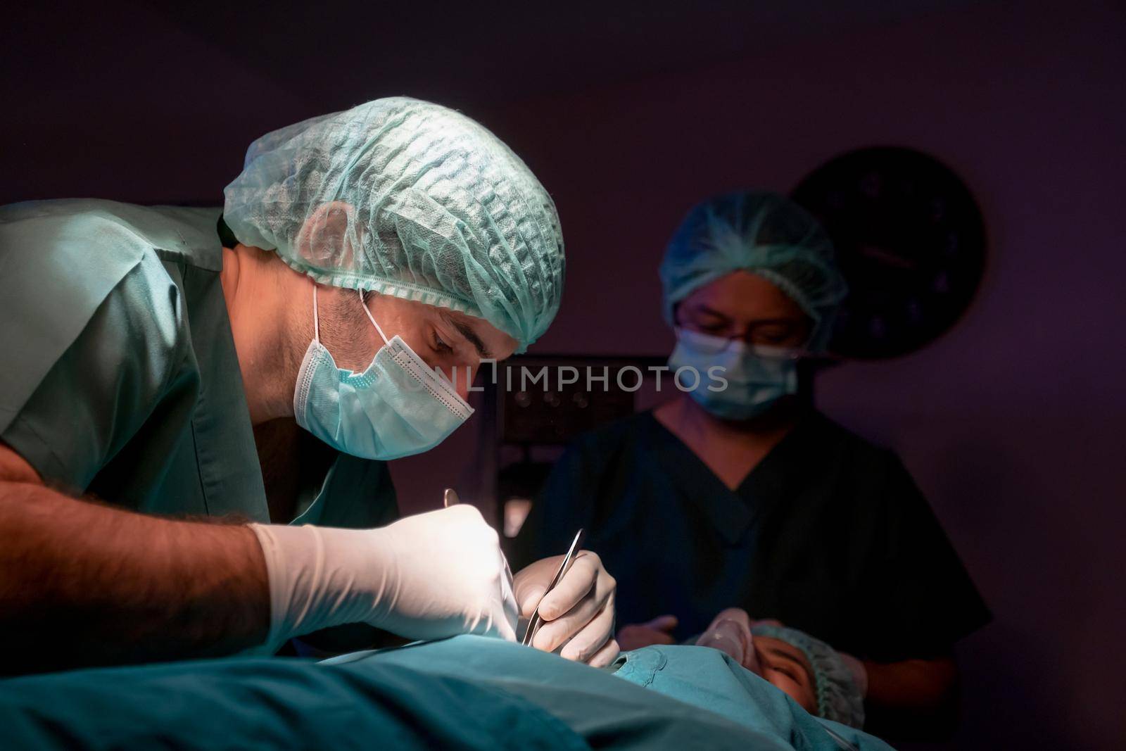 Operating doctor work on operation of patient with his staff stand to support near him in operating room of clinic or hospital.