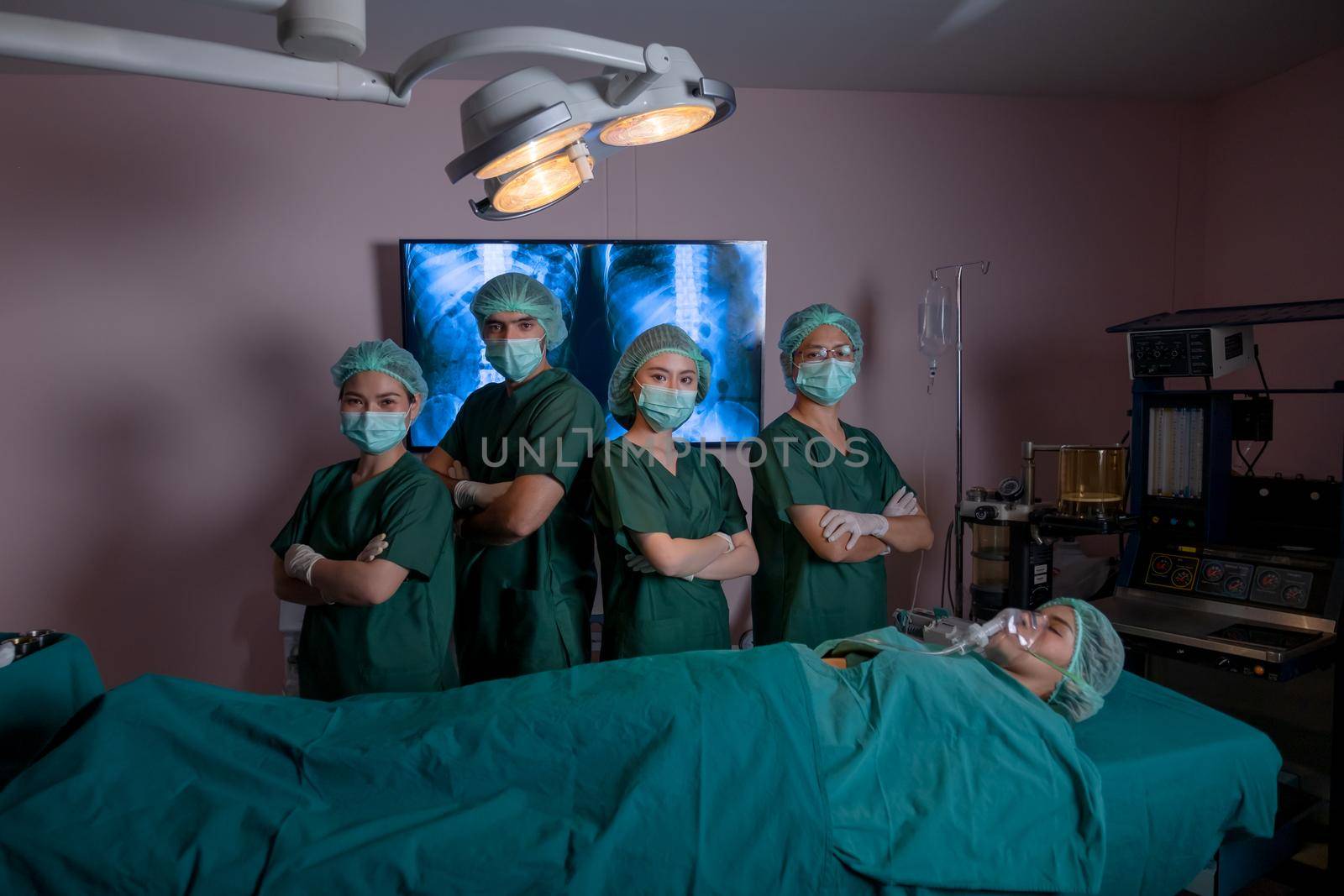 Operating team with doctor and nurse stand with arm-crossed confidence action in operating room and patient lie on bed. Teamwork for health care system support treatment of disease concept.