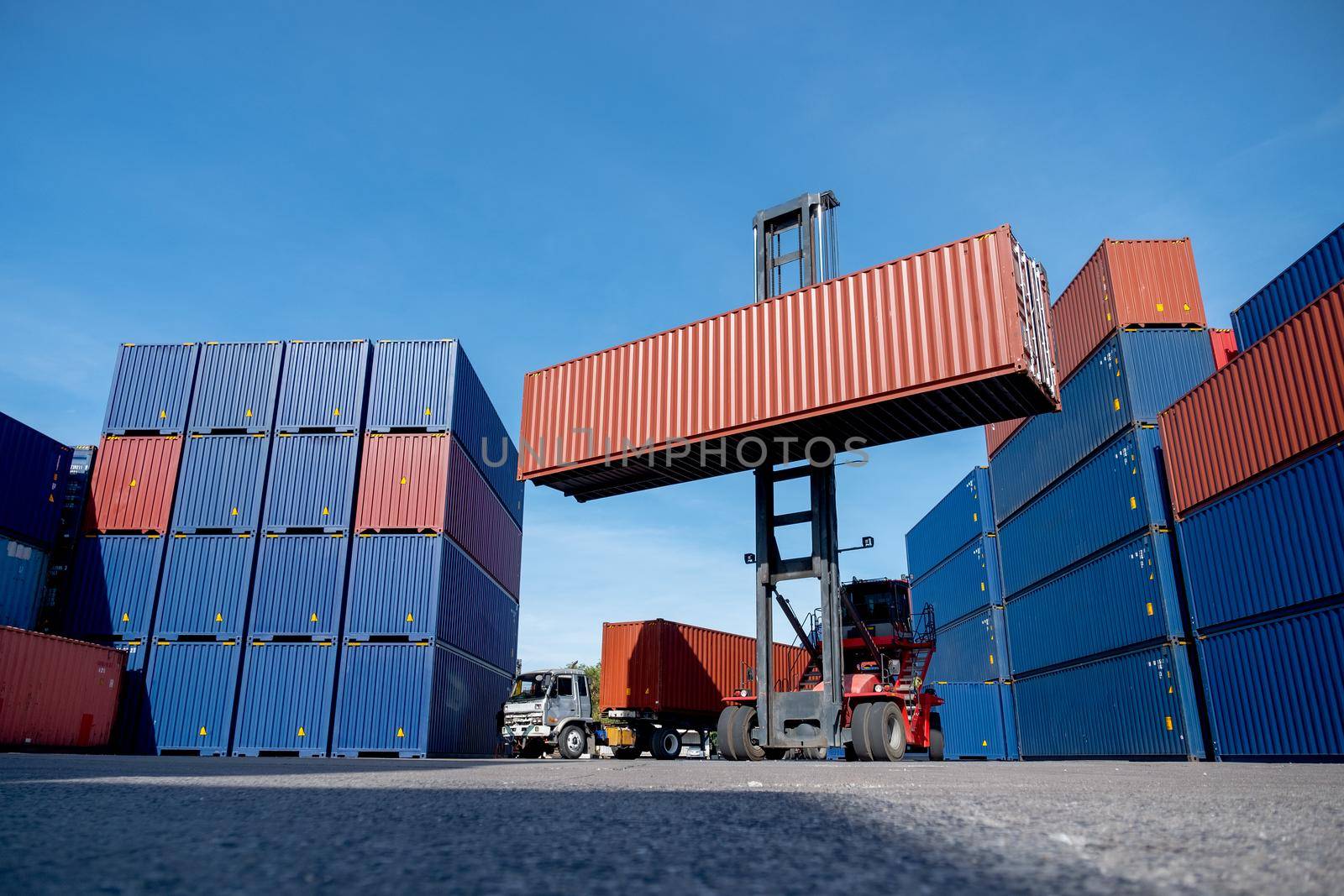 Wide shot of crane truck level up cargo container tank also show stack or layer of containers with different color, blue and brown with carrier truck as back of crane,  logistic and delivery concept.