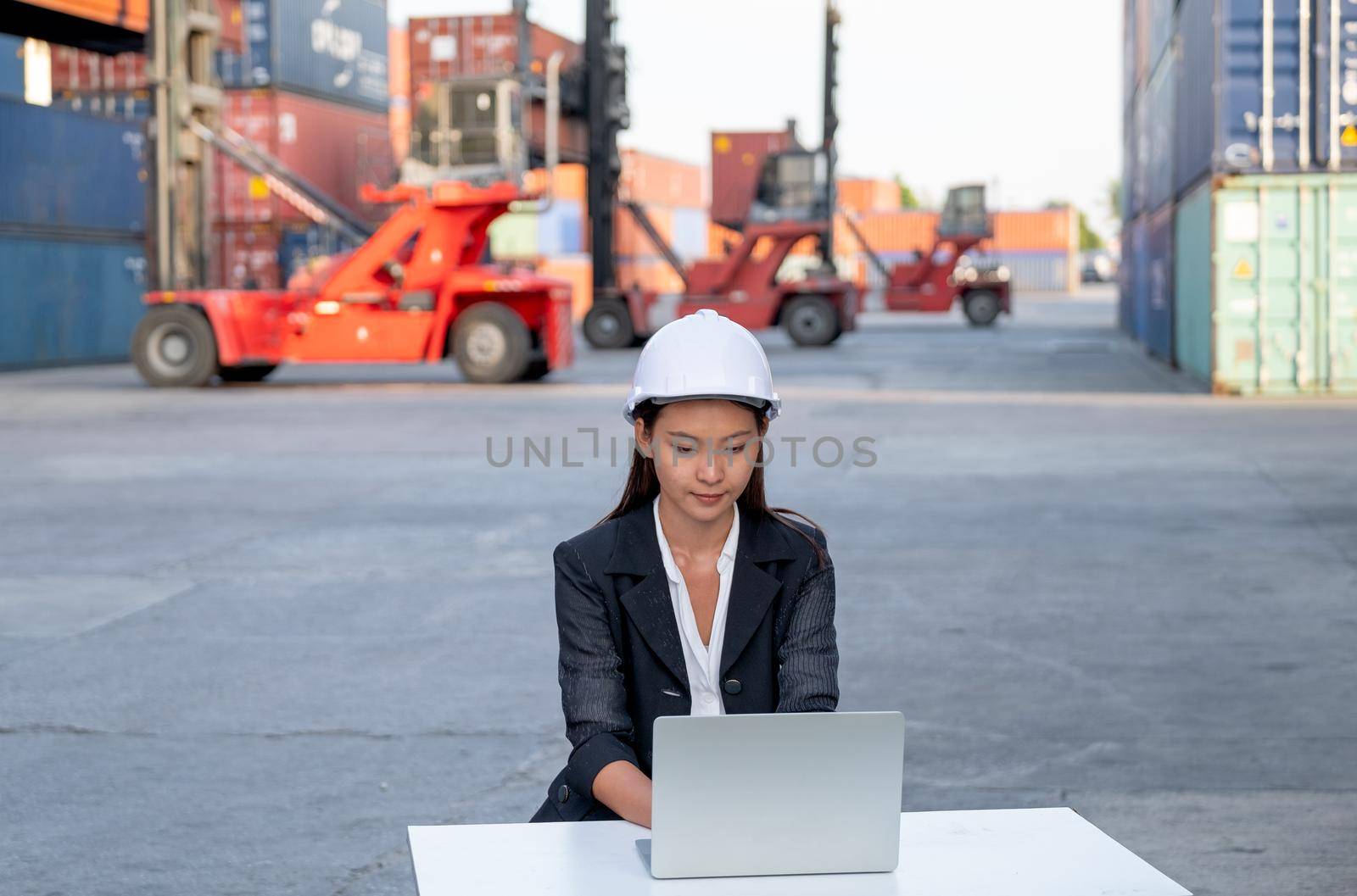 Asian cargo container worker of engineer woman use laptop in workplace area with concept of quality control for industrial business.