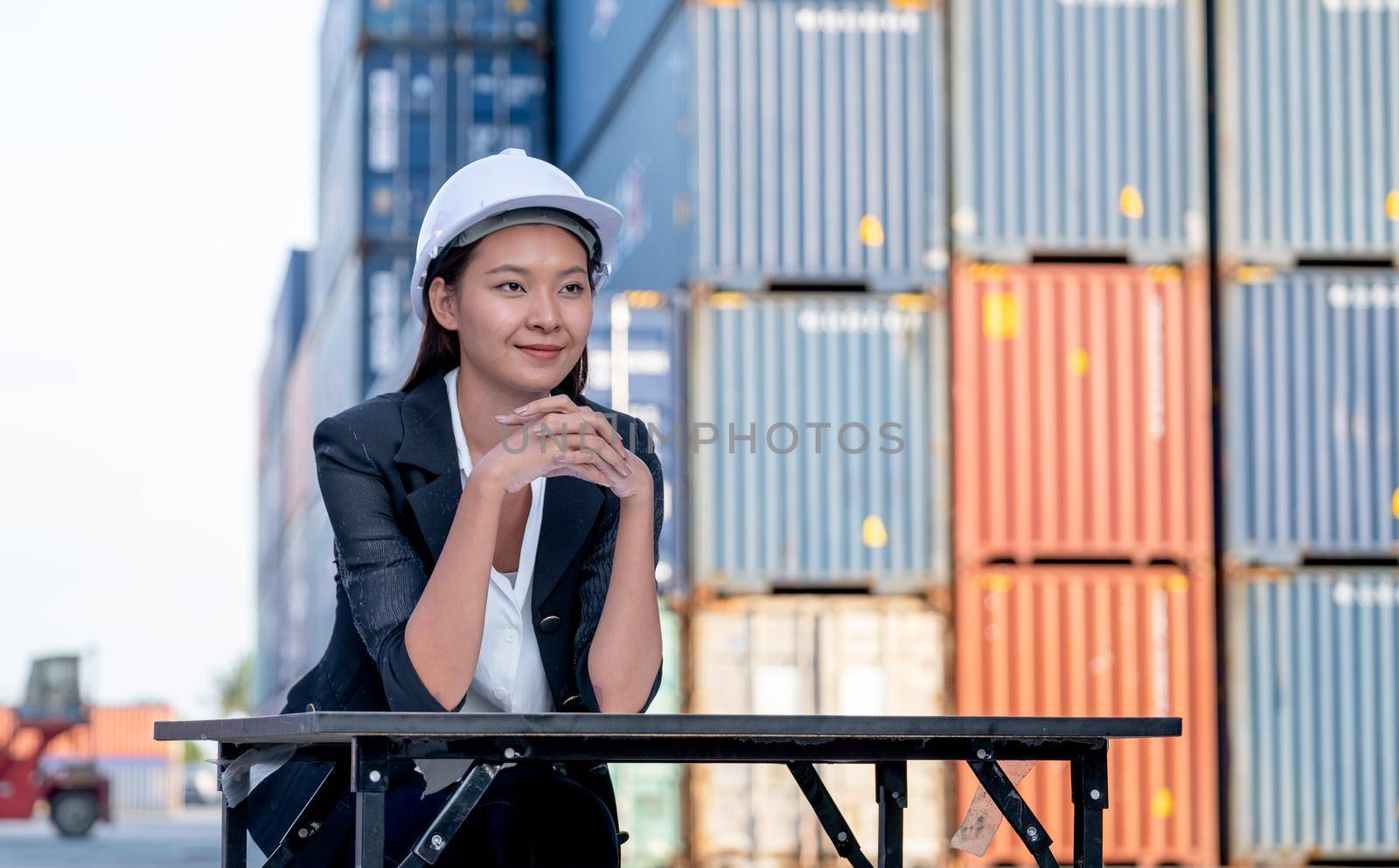 Portrait of engineer worker of factory technician with Chinese woman style sit in front of cargo container crane in workplace area. Concept of good support best successful for industrial business.