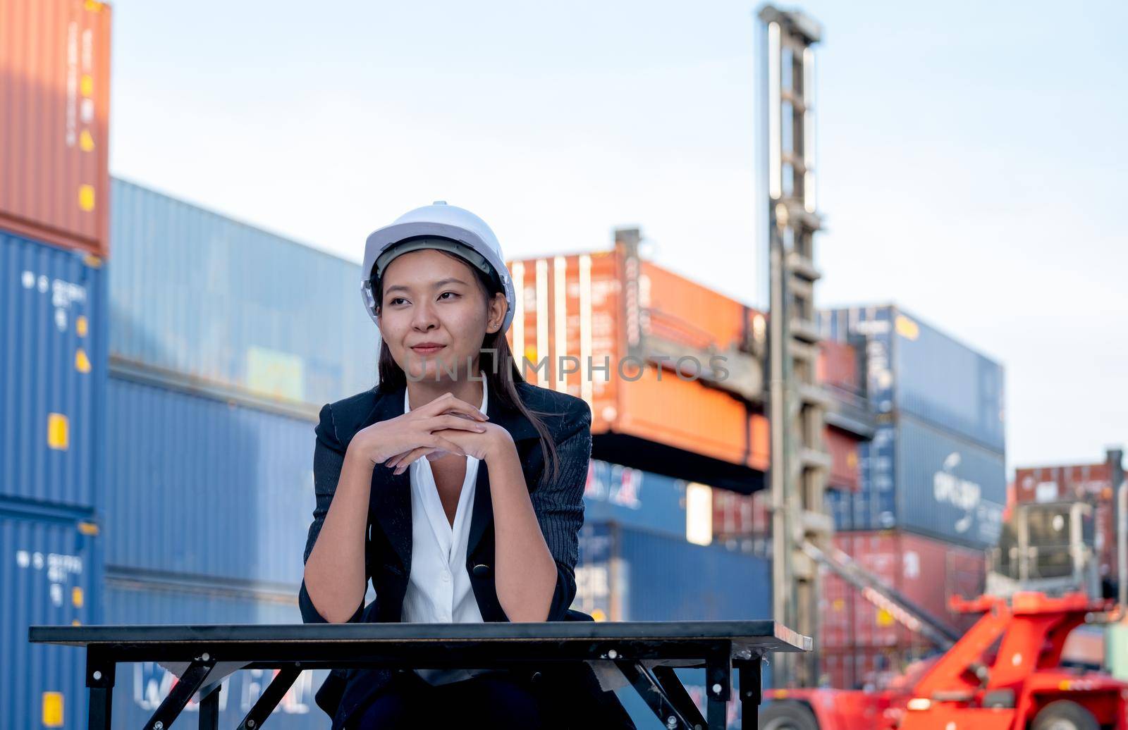 Portrait of engineer worker of factory technician with Chinese woman style sit in front of cargo container crane in workplace area. Concept of good support best successful for industrial business.