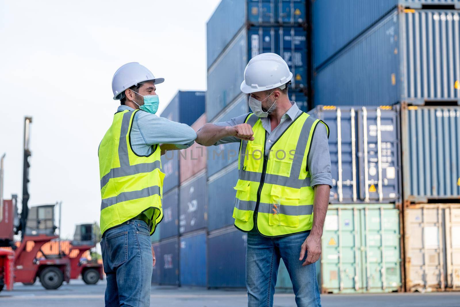 Two cargo container workers or engineer men show greeting together with new normal style by touching their elbow in workplace area. Concept of new normal lifestyle during pandemic of Covid-19 virus.