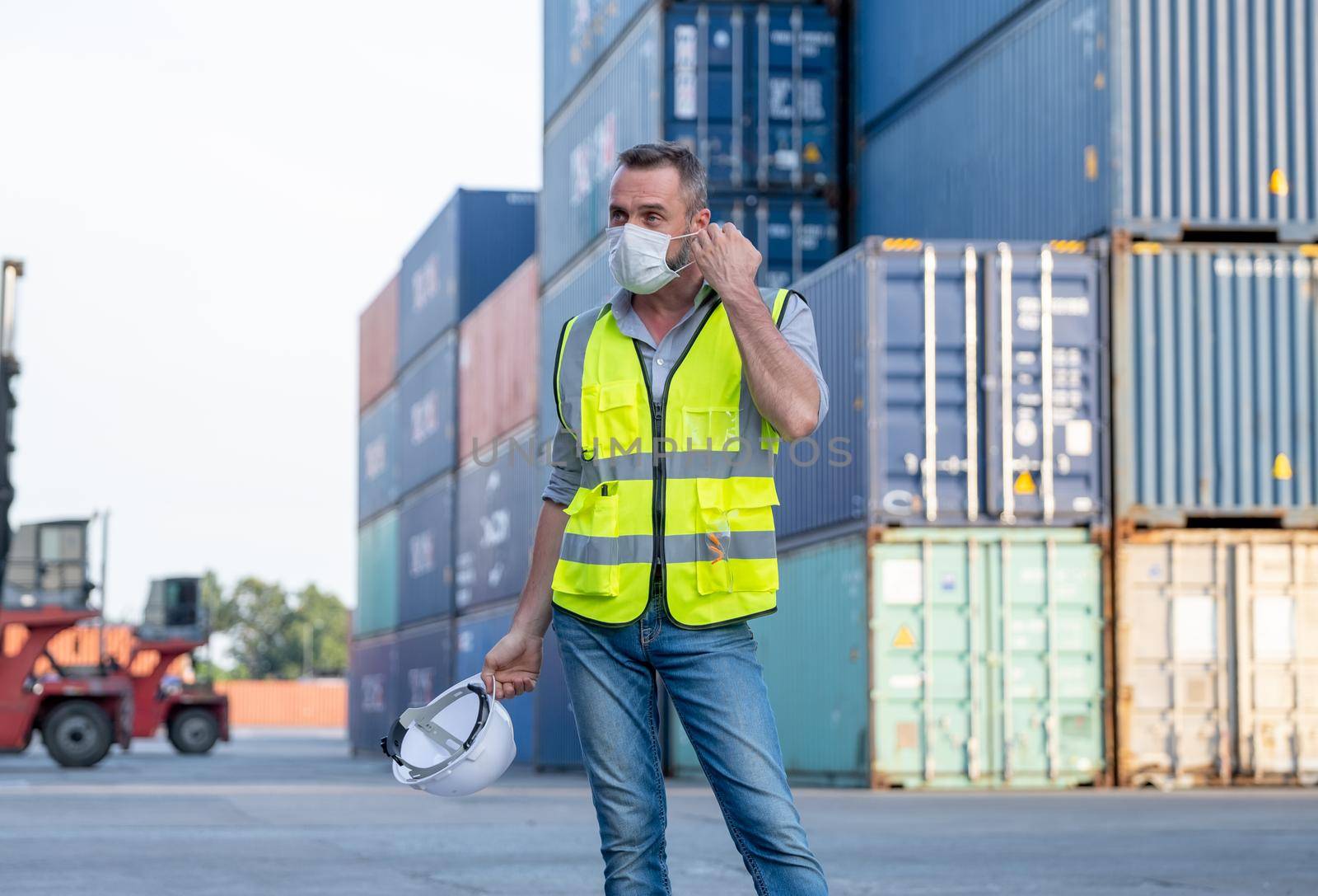 Factory of cargo container worker man take of mask and hardhat after finish work. Concept of new normal lifestyle in industrial business during pandemic of Covid-19 coronavirus in city.