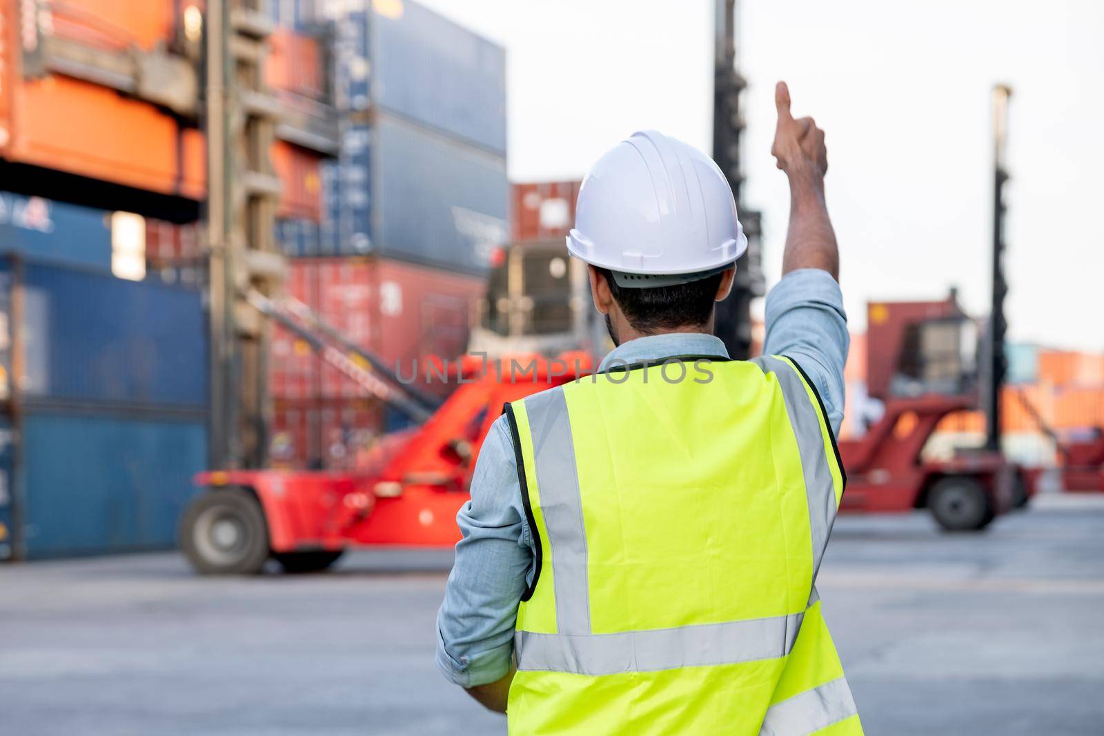 Back of foreman or cargo container worker show thumbs up to other co-worker who control crane truck in workplace area. Logistic and shipyard transportation for delivery system concept. by nrradmin