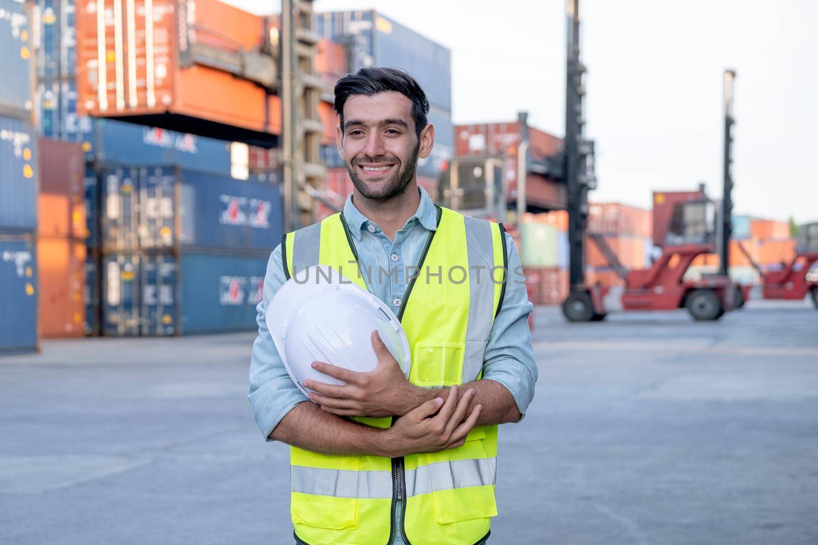 Portrait of engineer worker of factory technician stand with happy emotion and in front of cargo container crane in workplace area. Concept of good support best successful for industrial business.