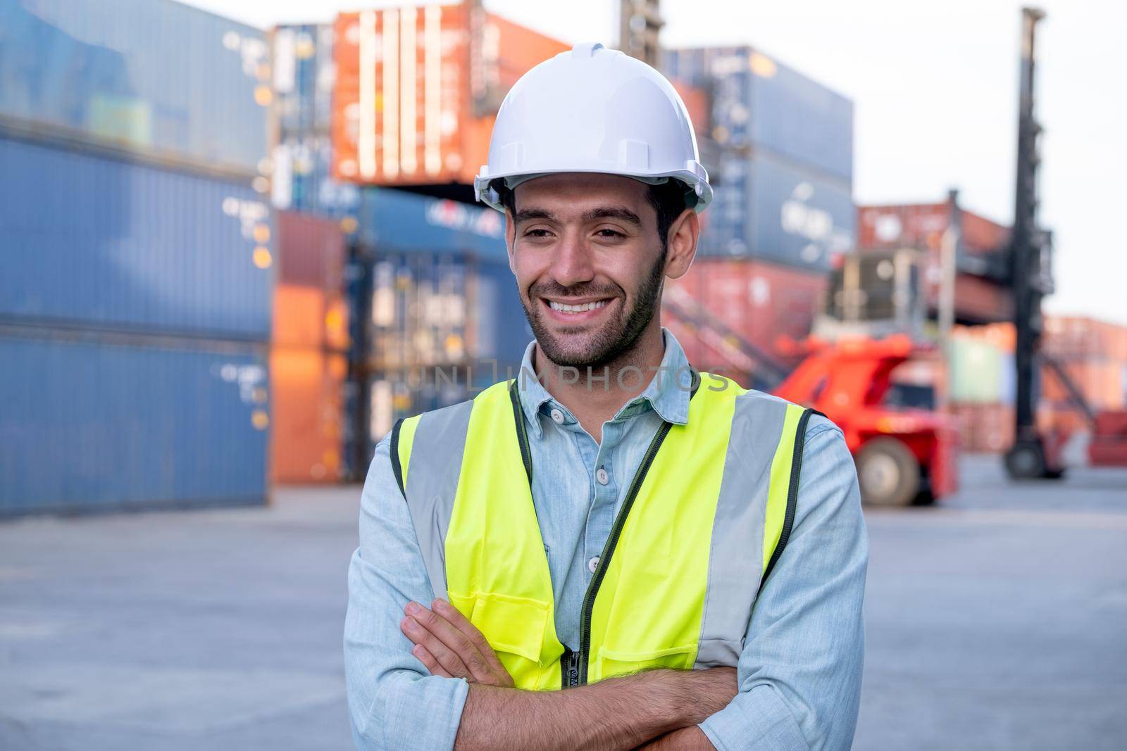 Portrait of engineer worker of factory technician stand with happy emotion and in front of cargo container crane in workplace area. Concept of good support best successful for industrial business.