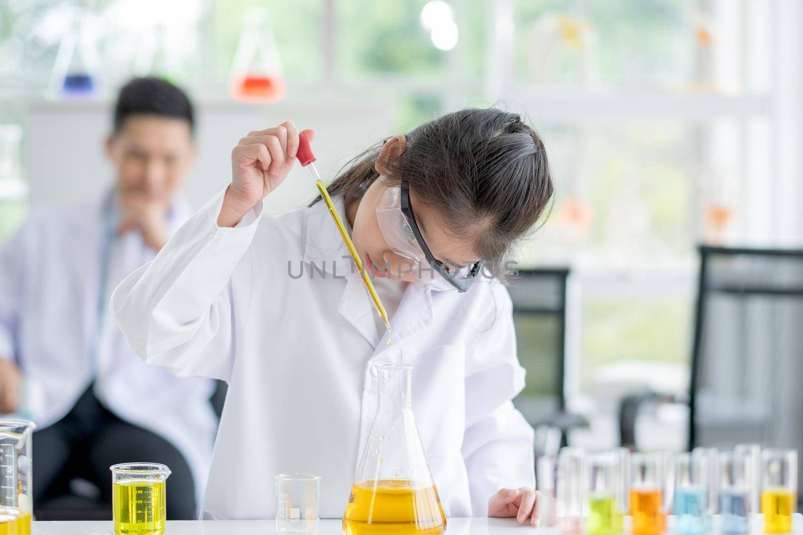 Lovely little girl scientist enjoy and concentrate to examine the color chemical in laboratory by using dropper with day light. Concept of good practice and education of science for children support.