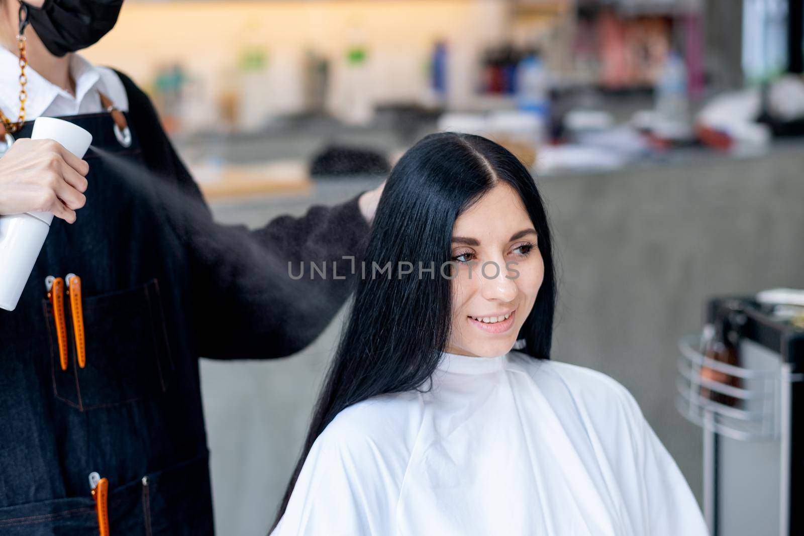 Caucasian woman is spraying with haircare product by beauty salon barber and she smile with relax and happy emotion in the shop.