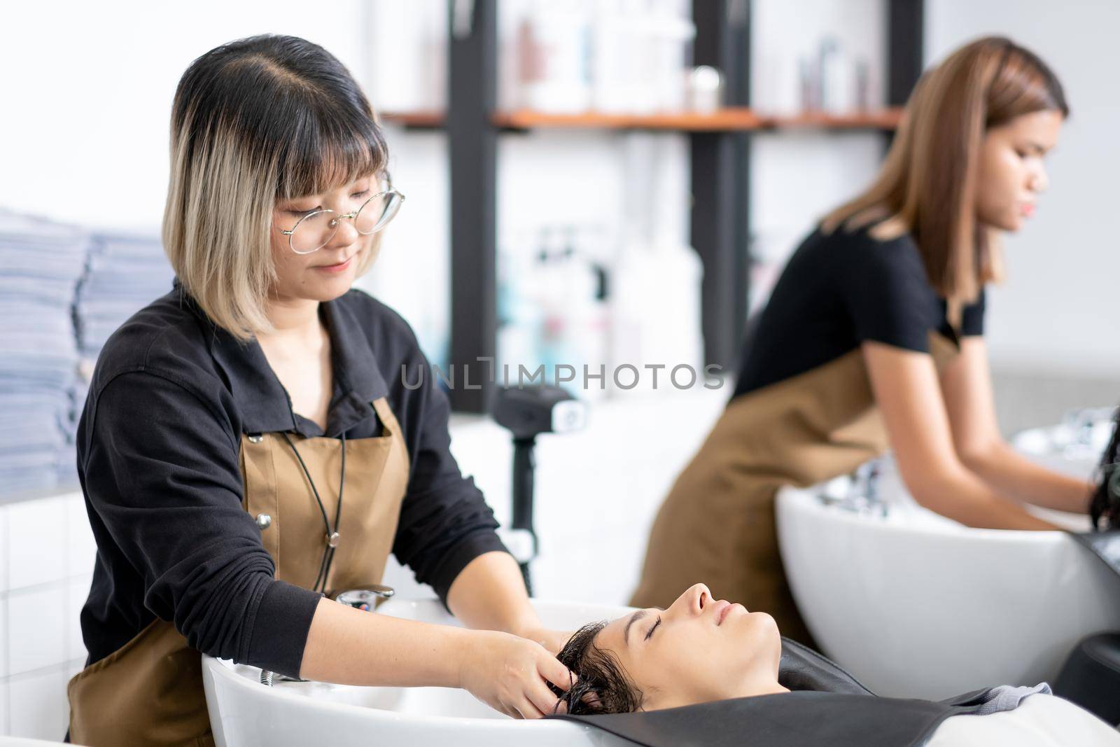 Beautiful woman is washed her hair by young barber girl in beauty salon shop and she look relax and happy. Beauty hair and body care business for good appearance concept. by nrradmin