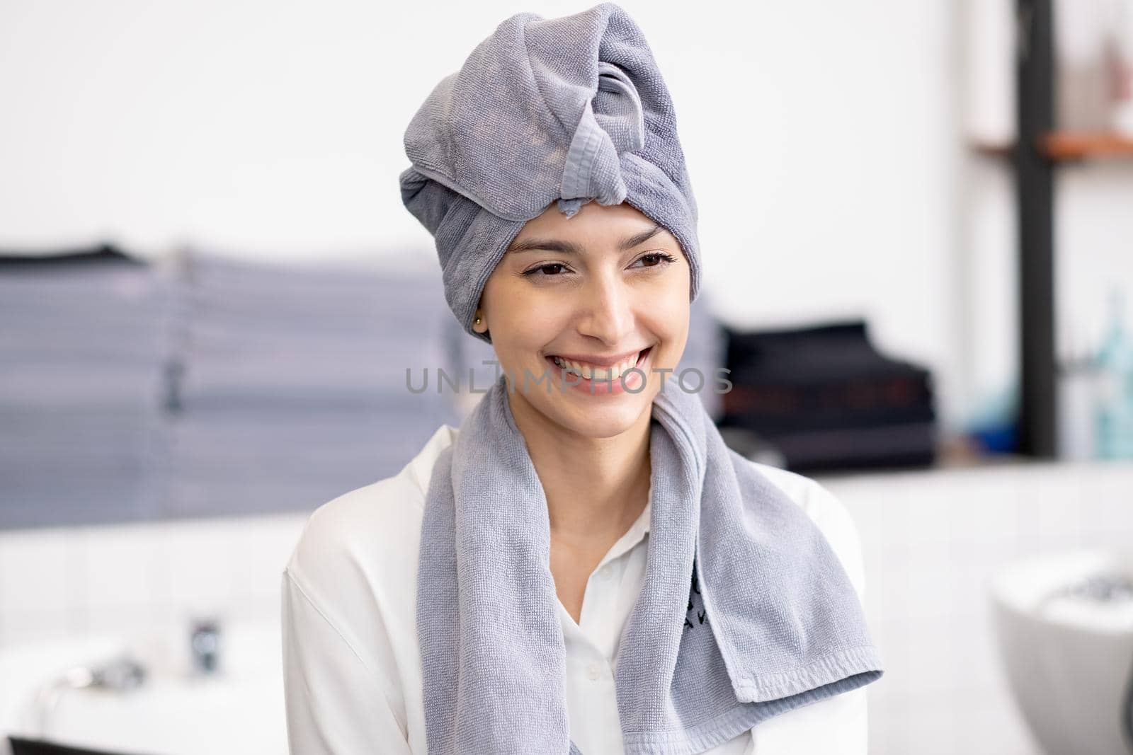 Portrait of beautiful Caucasian woman with towel to cover her head and hair is smiling look to the right side and stay in beauty salon shop.