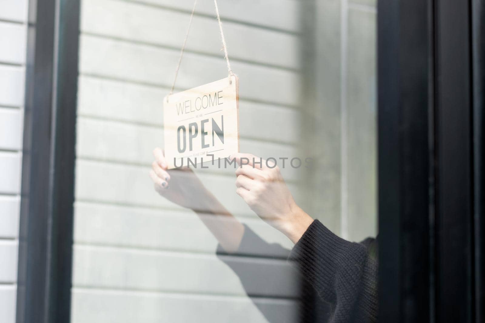 Close up hands hold banner of word, open, in front the shop to notice and invite people to go inside and get service.