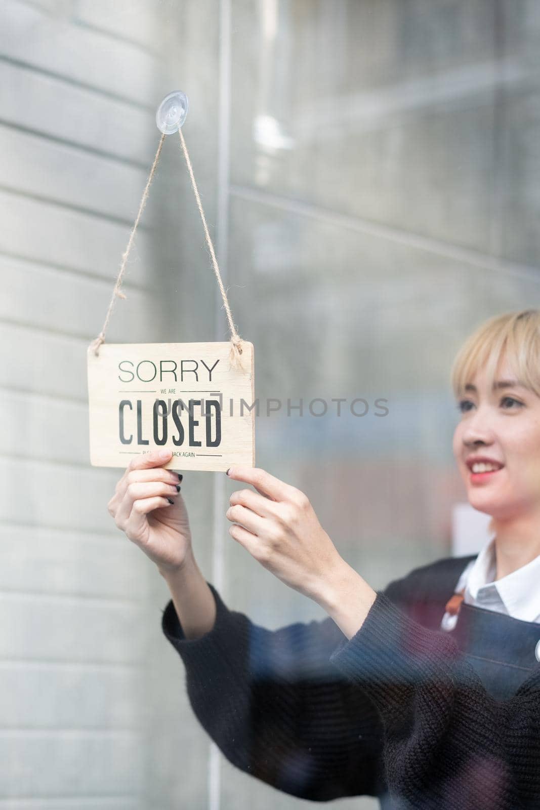 Banner of word, Closed, is held by beautiful Asian woman after finish work or during pandemic of Covid-19 in the city.