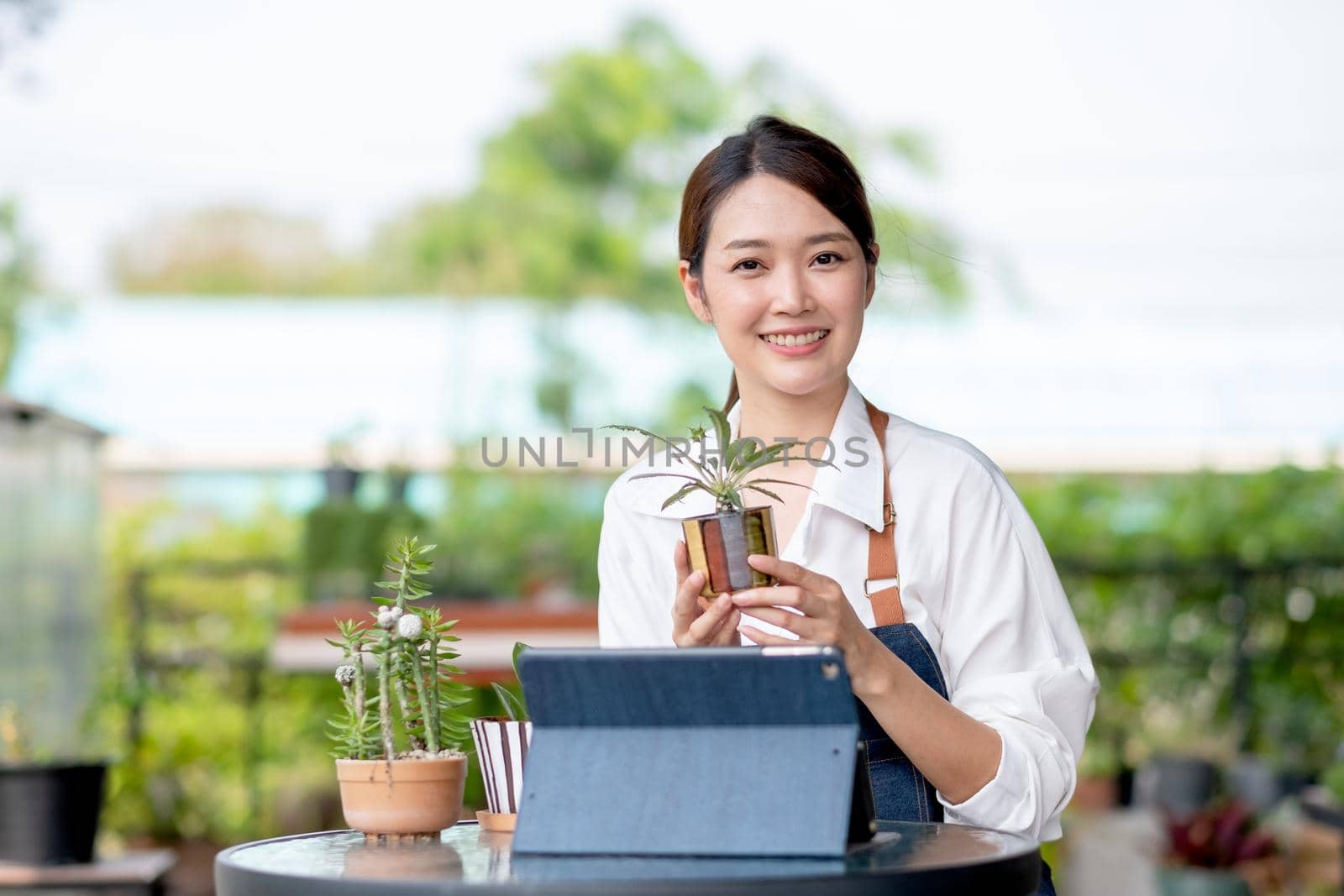 Beautiful Asian girl hold flora pot and look at camera with happy emotion. Sustainable with small business work involve with plant of flora concept.