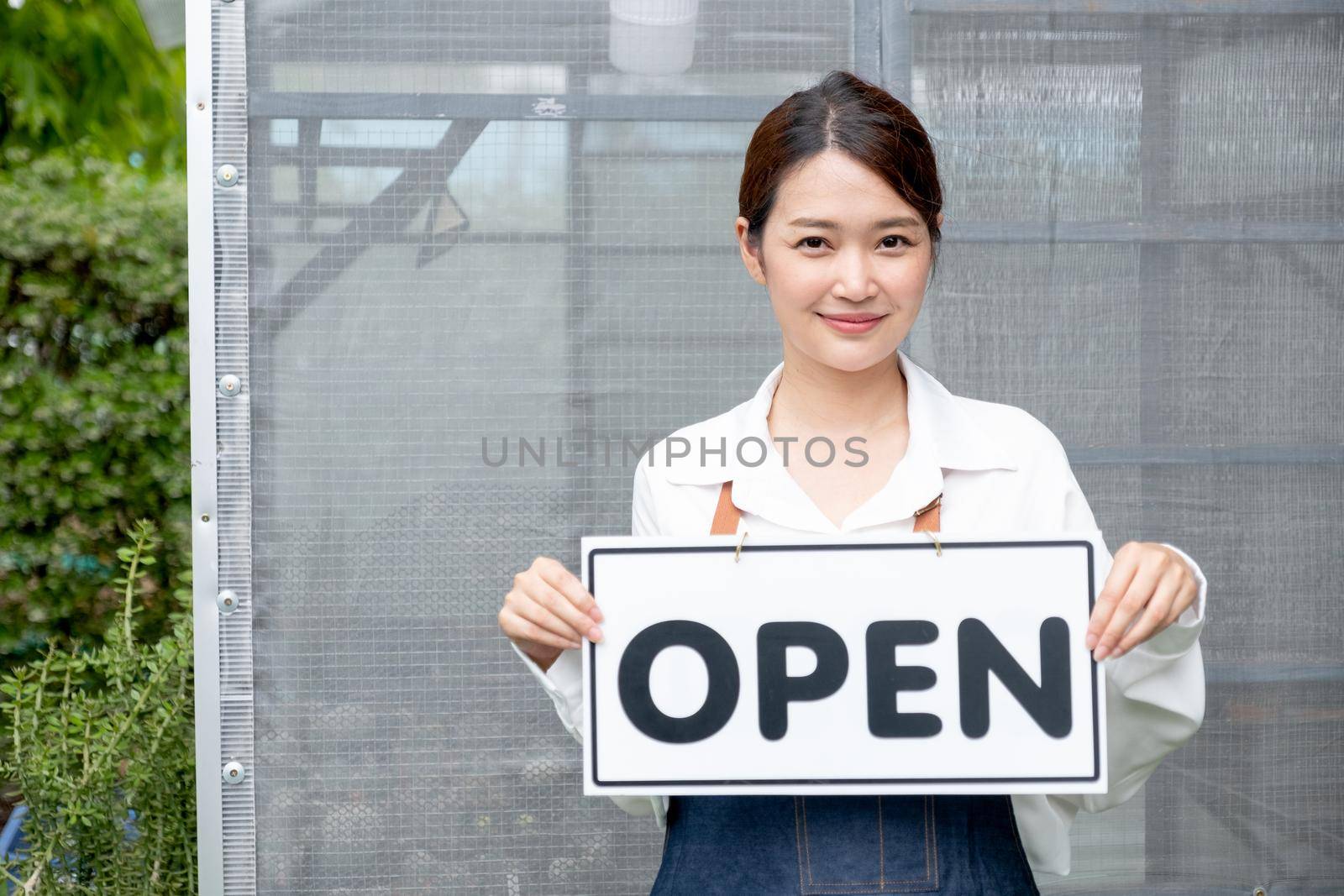 Beautiful Asian woman present banner with word open in front of green house and happy emotion relate with re-open the business with sustainable activity.