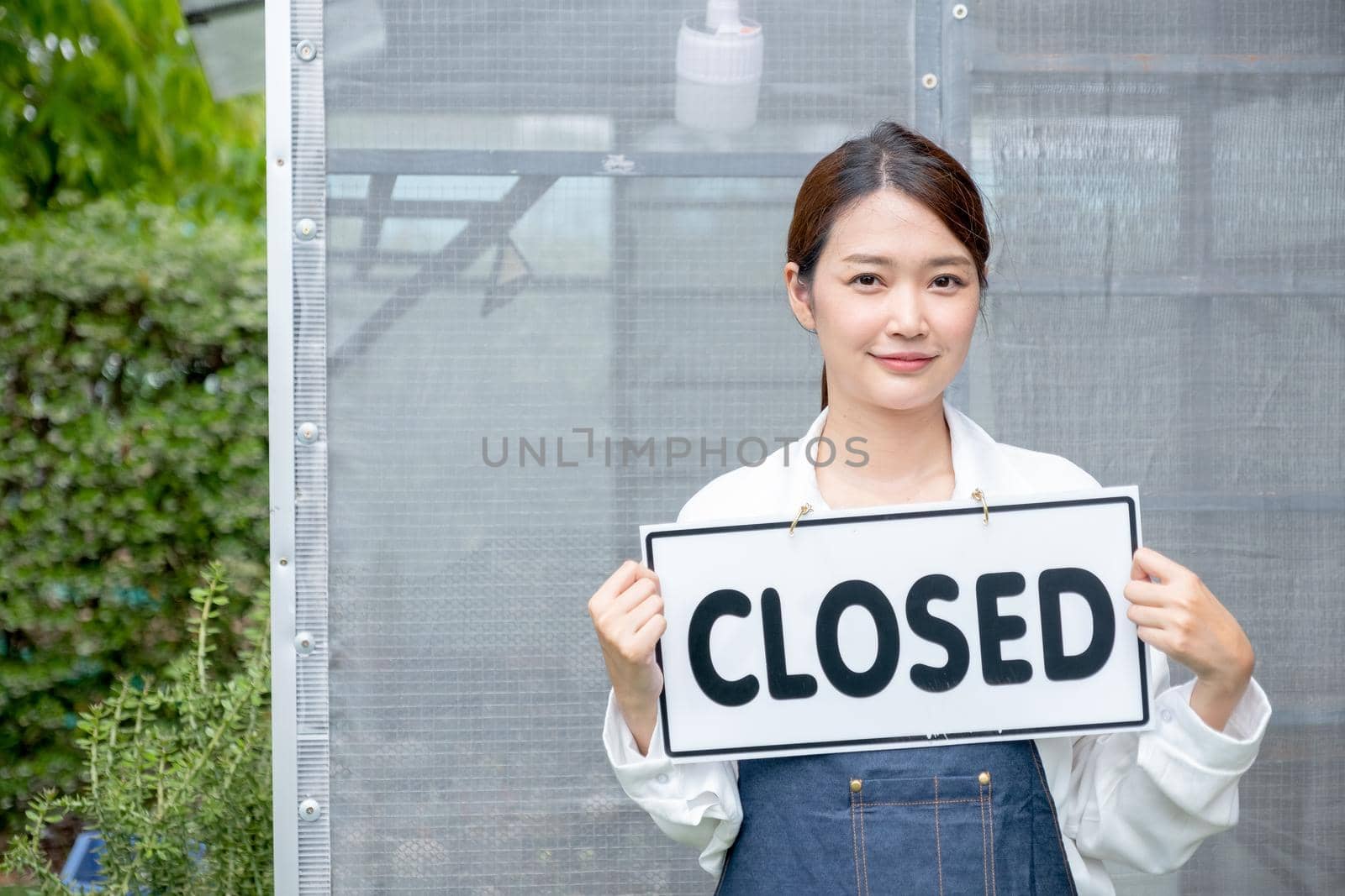 Beautiful Asian woman present banner with word closed in front of green house and sad emotion relate with close the business of sustainable activity.