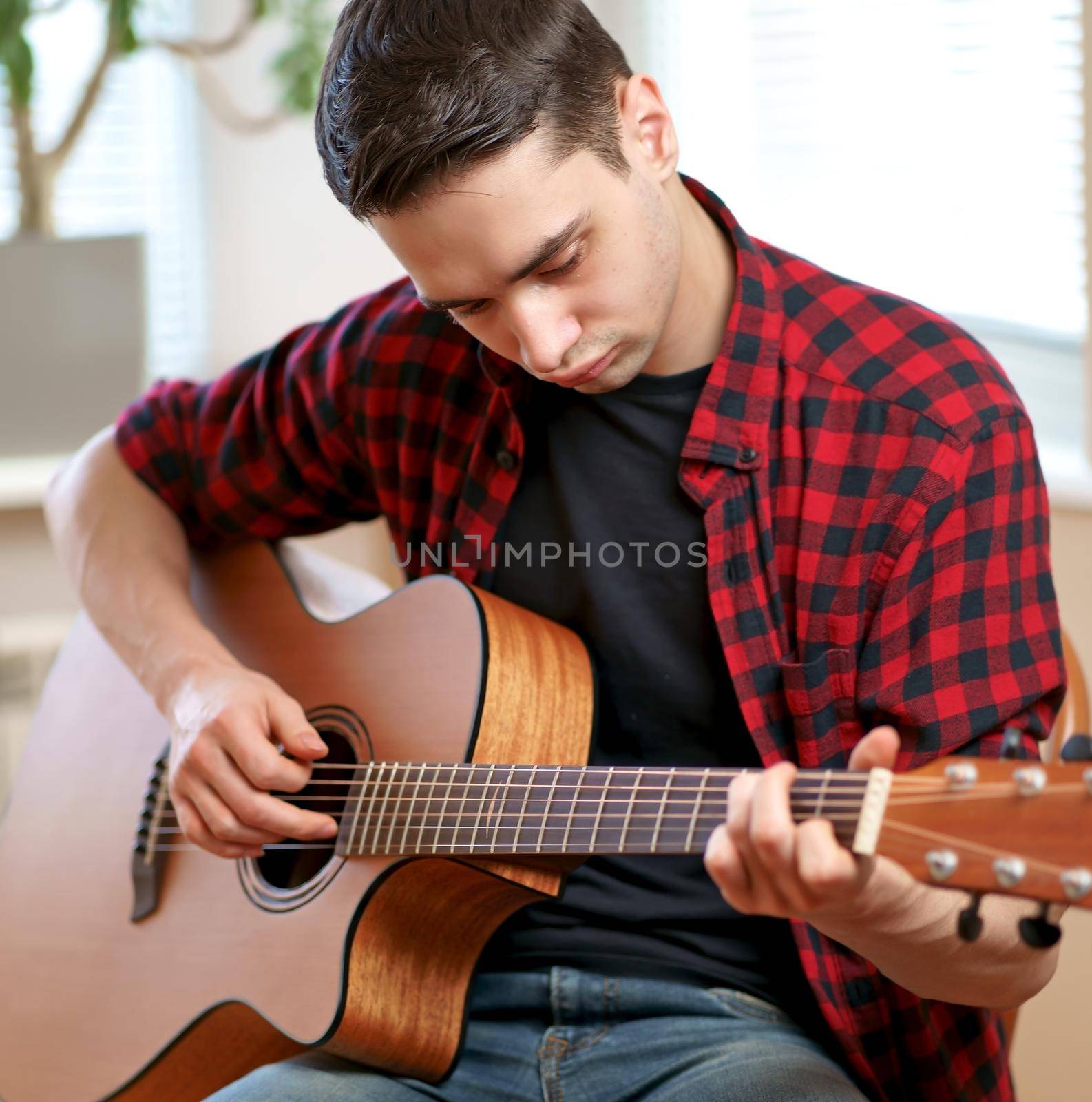 A young man learns to play the guitar using the Internet, laptop, online lesson. Hobby and leisure concept by aprilphoto