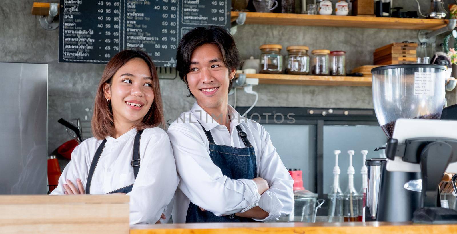 Two Asian barista or coffee maker man and woman stand with arm-crossed or confidence action also look to each other and smile in cafe shop. Concept of happy working with small business together.