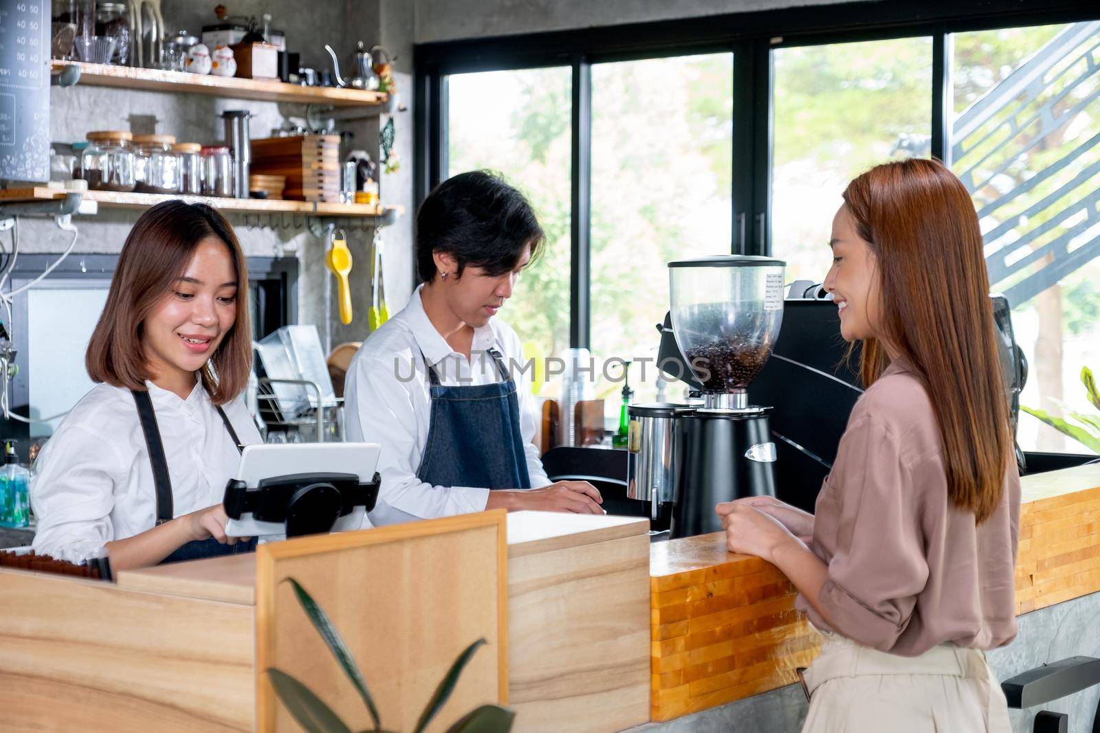 Asian barista or coffee maker receive the order from customer woman while her co-worker prepare coffee by machine. Concept of good teamwork support small business system.