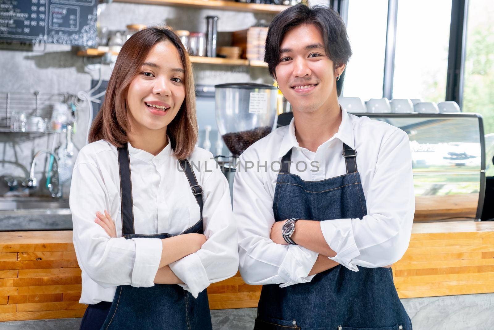 Asian barista or coffee maker man and woman stand with arm-crossed or confidence action also look to camera and smile in coffee shop.