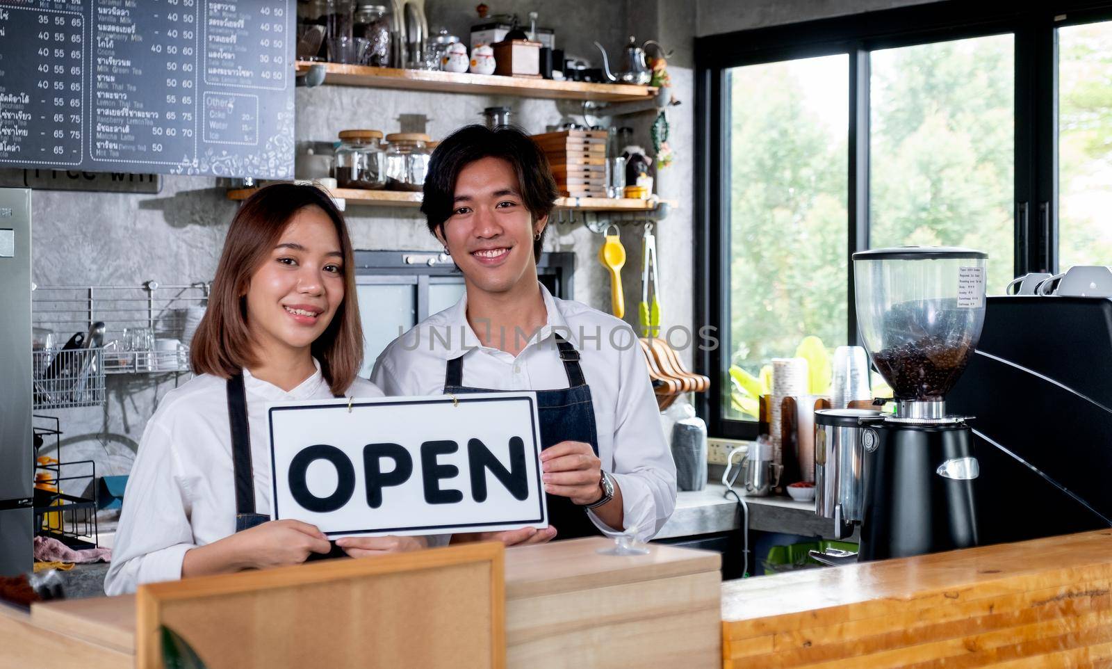 Two barista or coffee maker man and woman hold banner of open for the symbol of ready to service for customer in coffee shop. Concept of happy working with small business and sustainable.